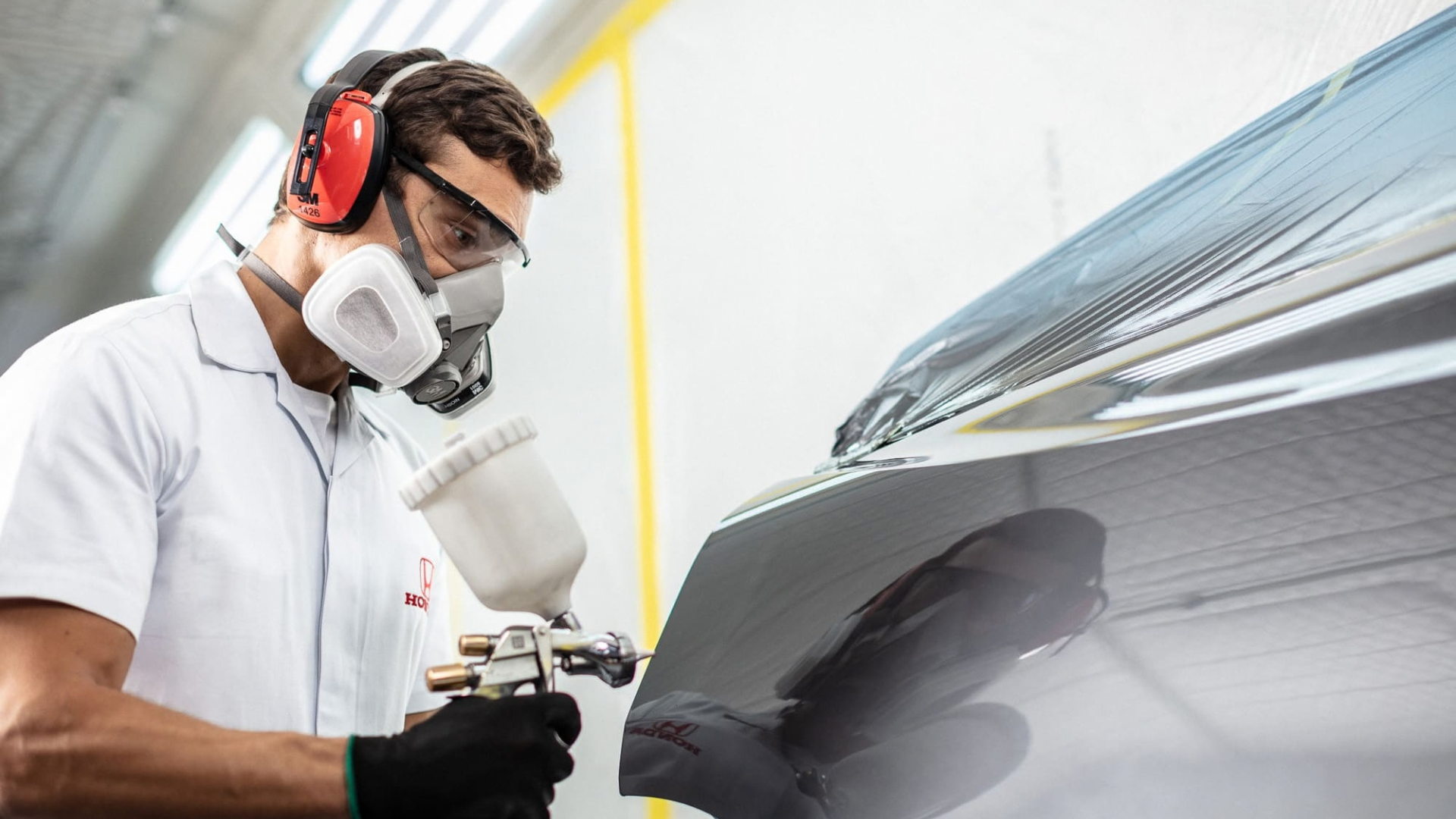 Technician in respirator and gloves inspecting a car panel in a spray booth