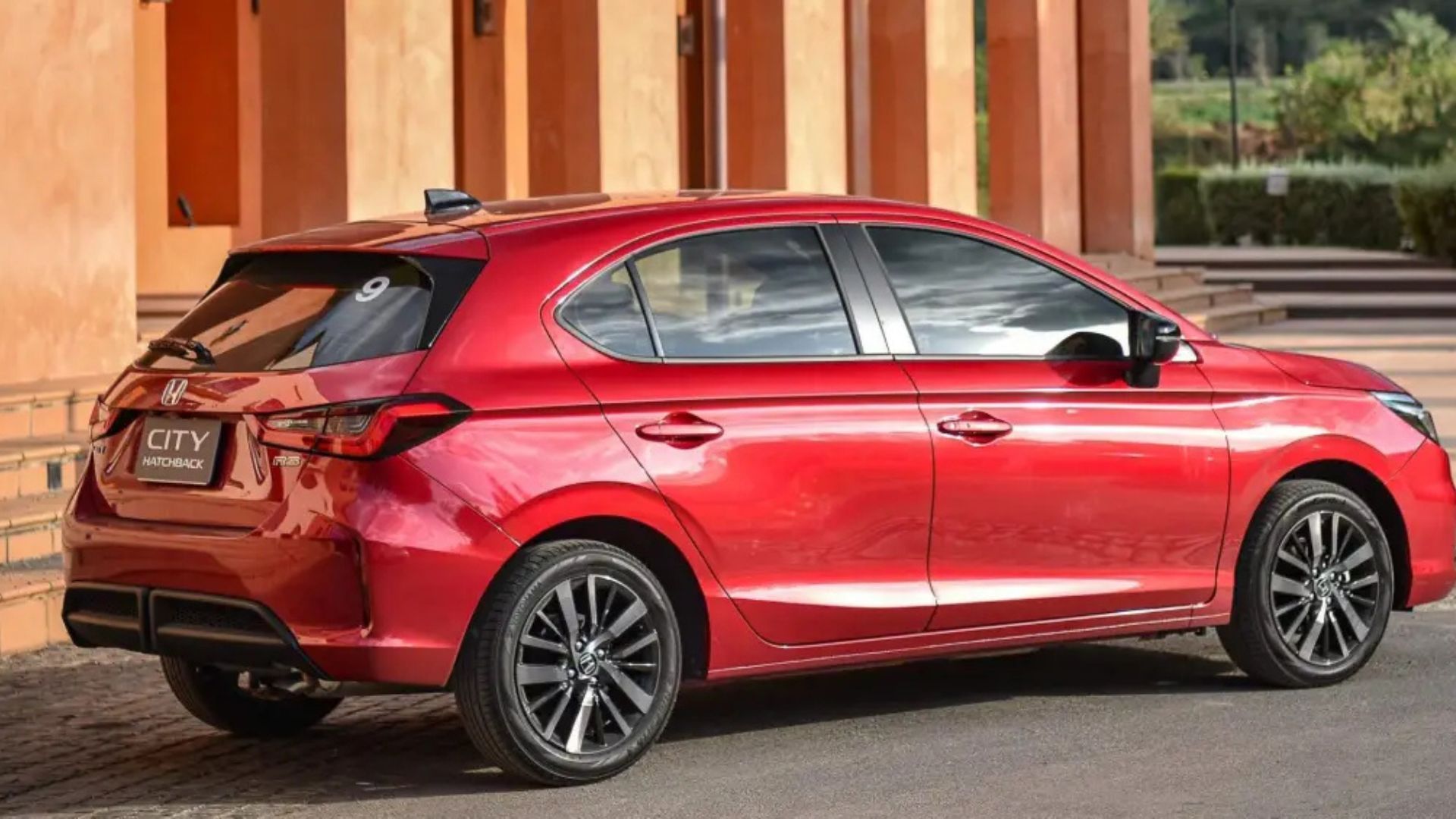 Red compact car parked by a tan building, side view on a street.