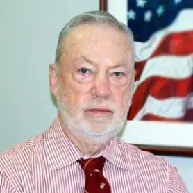 Man in red striped shirt and tie, with American flag in background