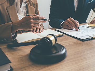 Lawyers signing documents at a desk with a gavel in the foreground