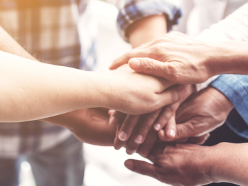 Hands stacked together in a team huddle indoors, with warm light in the background