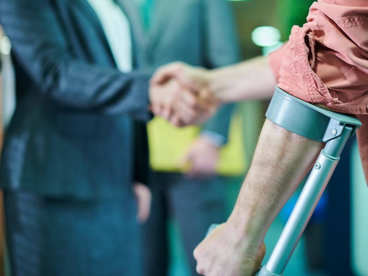 Two people shaking hands beside a person on crutches in a hospital hallway