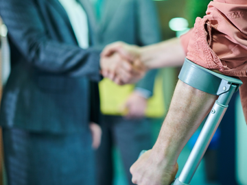 Two people shaking hands beside a person on crutches in a hospital hallway