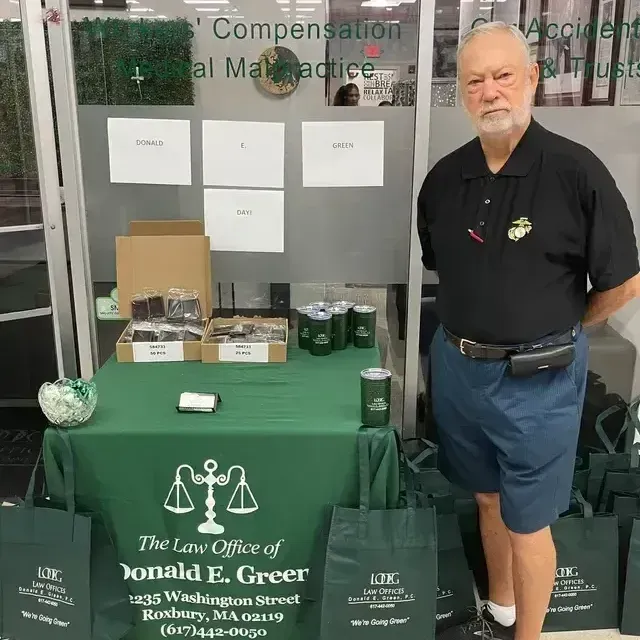 Man standing beside a green-draped law office display table with brochures and office items