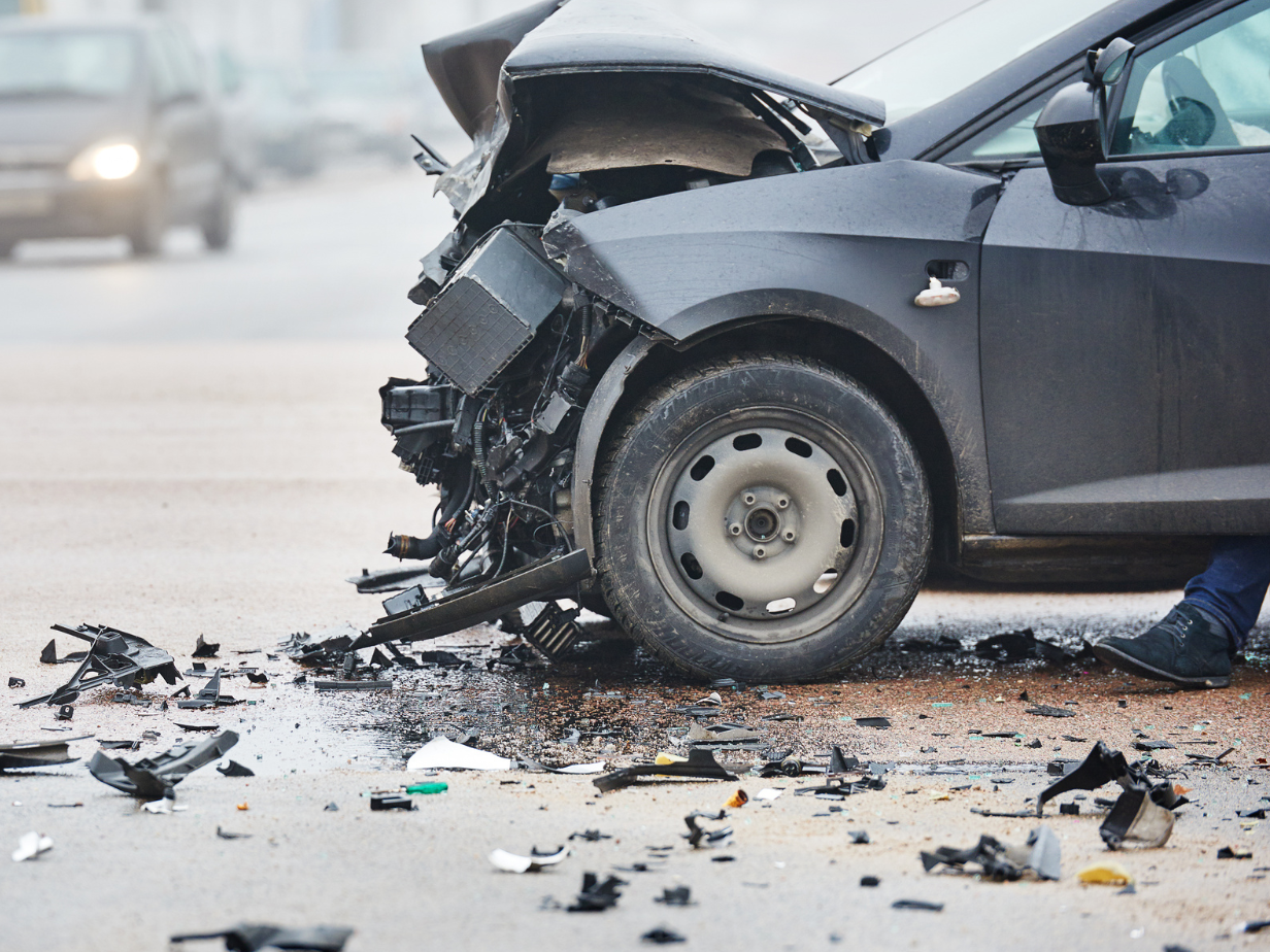 Severe car crash with a damaged black car’s front end and debris scattered on the road