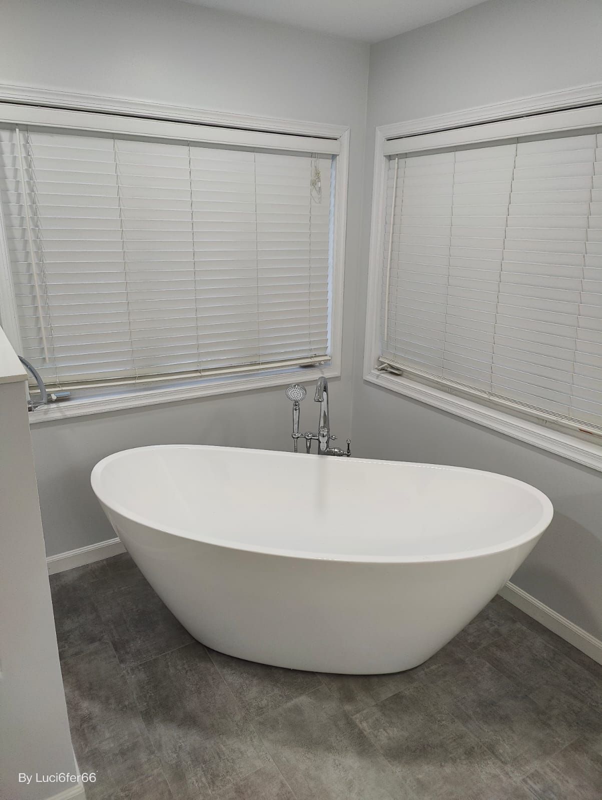 White freestanding bathtub in a gray corner bathroom with two windows and blinds