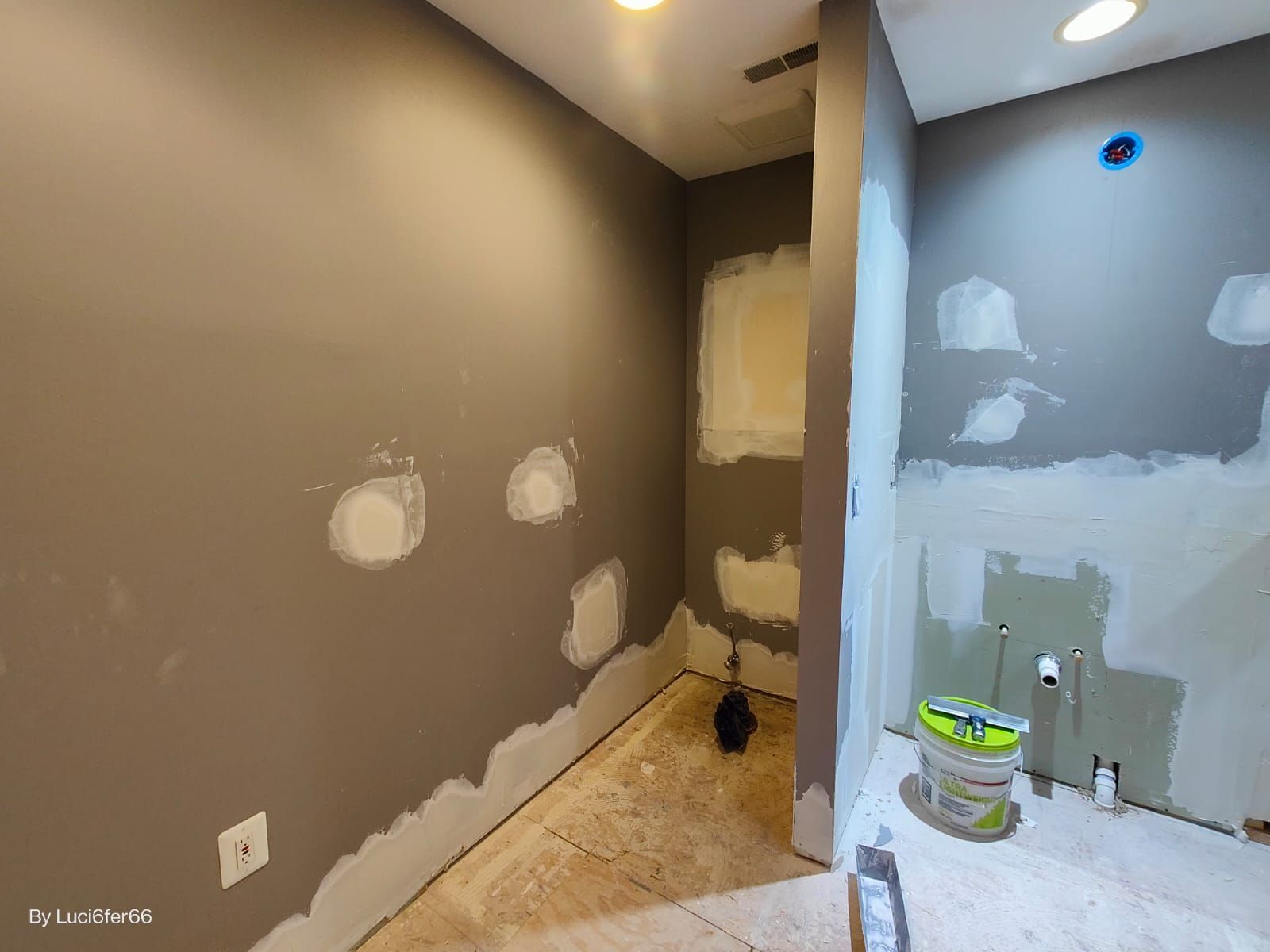 Partially renovated basement with gray walls, patchy drywall, a doorway, and painting supplies on the floor
