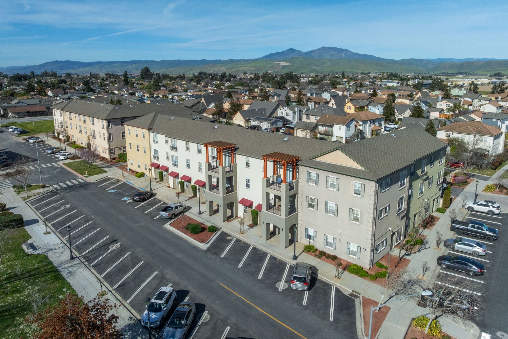 Aerial view of colorful apartment buildings beside a parking lot in a suburban neighborhood with hills in the distance