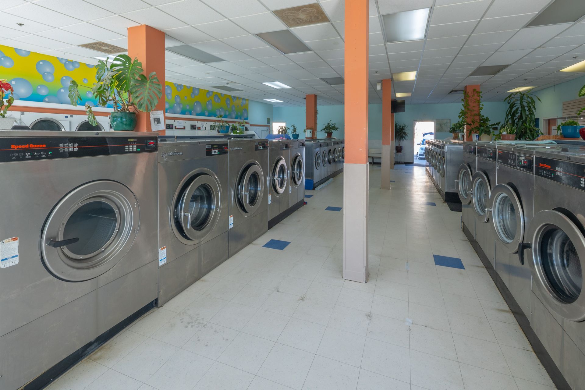 Bright laundromat with rows of silver washing machines and orange columns inside.