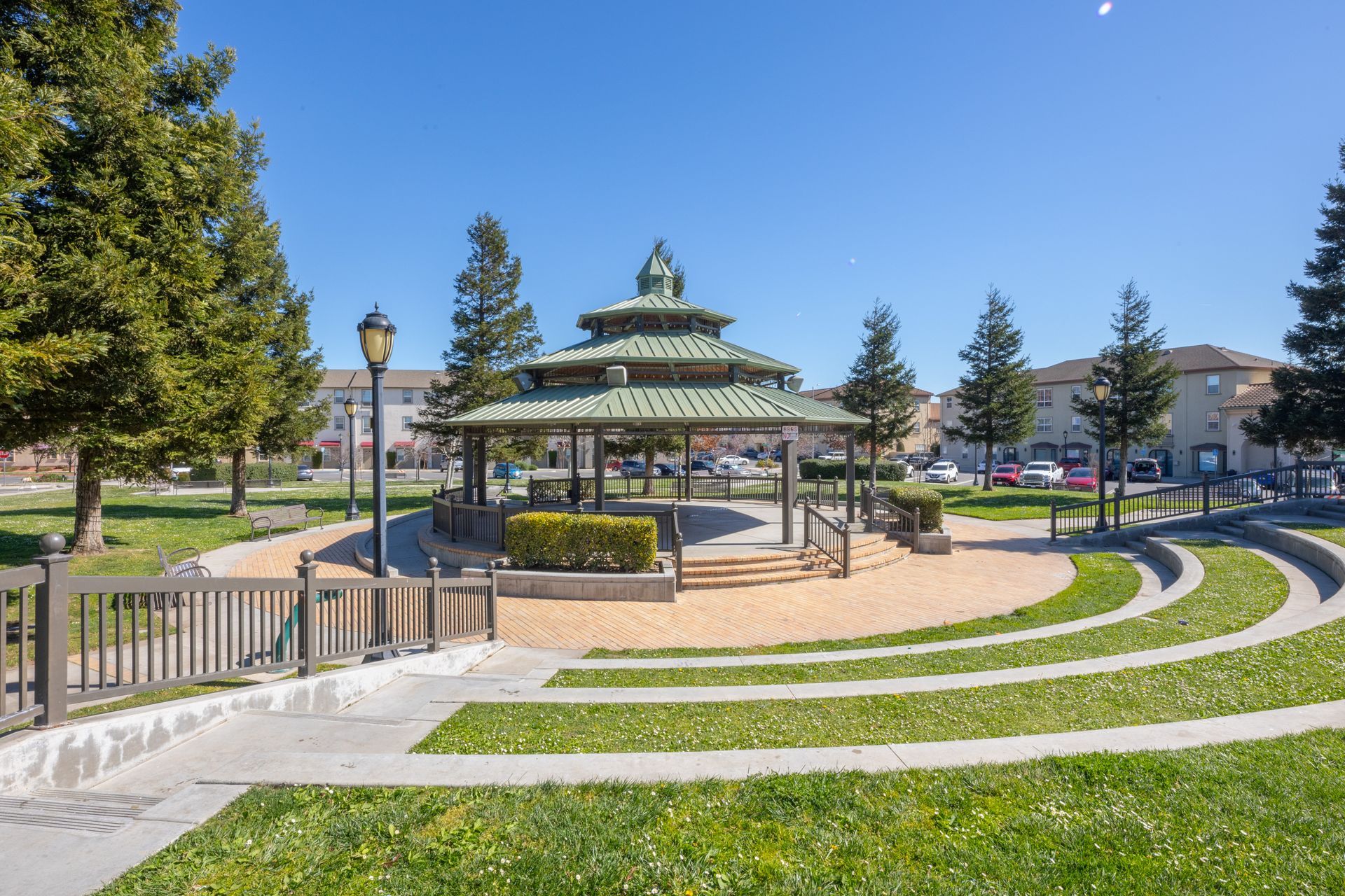 Gazebo in a landscaped park with curved concrete seating, green grass, trees, and a clear blue sky