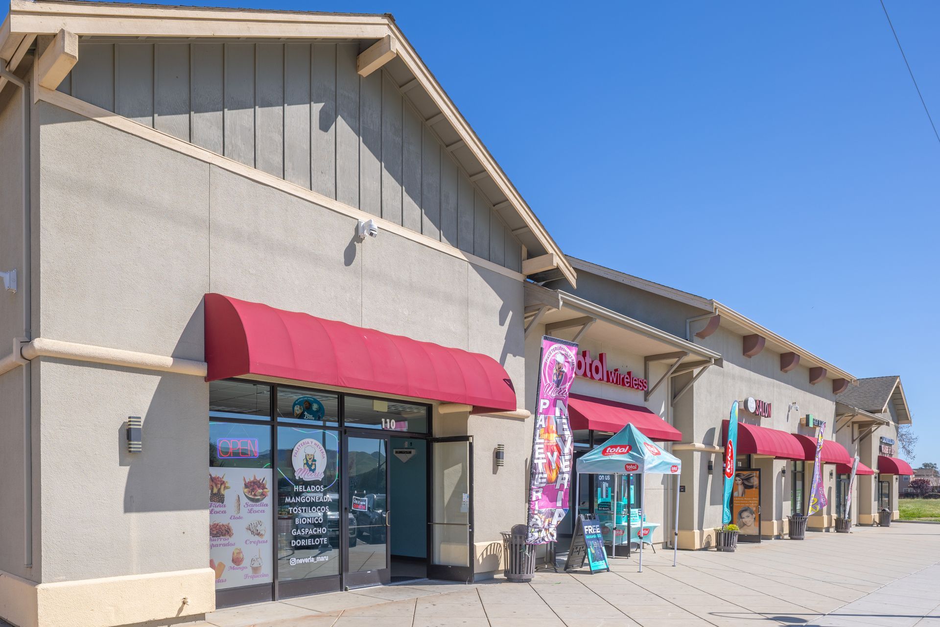 Row of storefronts with colorful awnings along a sunny shopping plaza