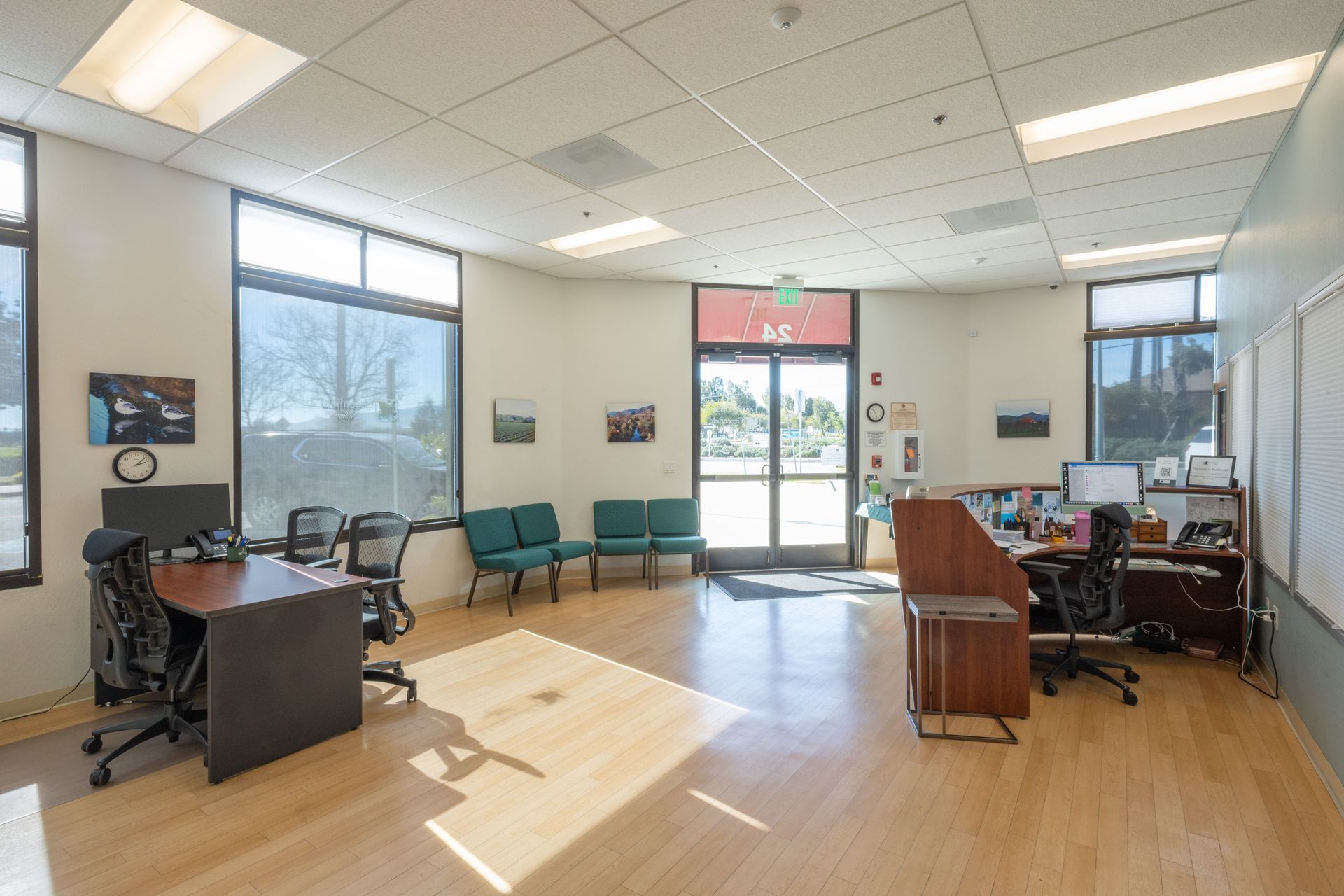 Bright office lobby with desks, chairs, large windows, and a glass entrance door