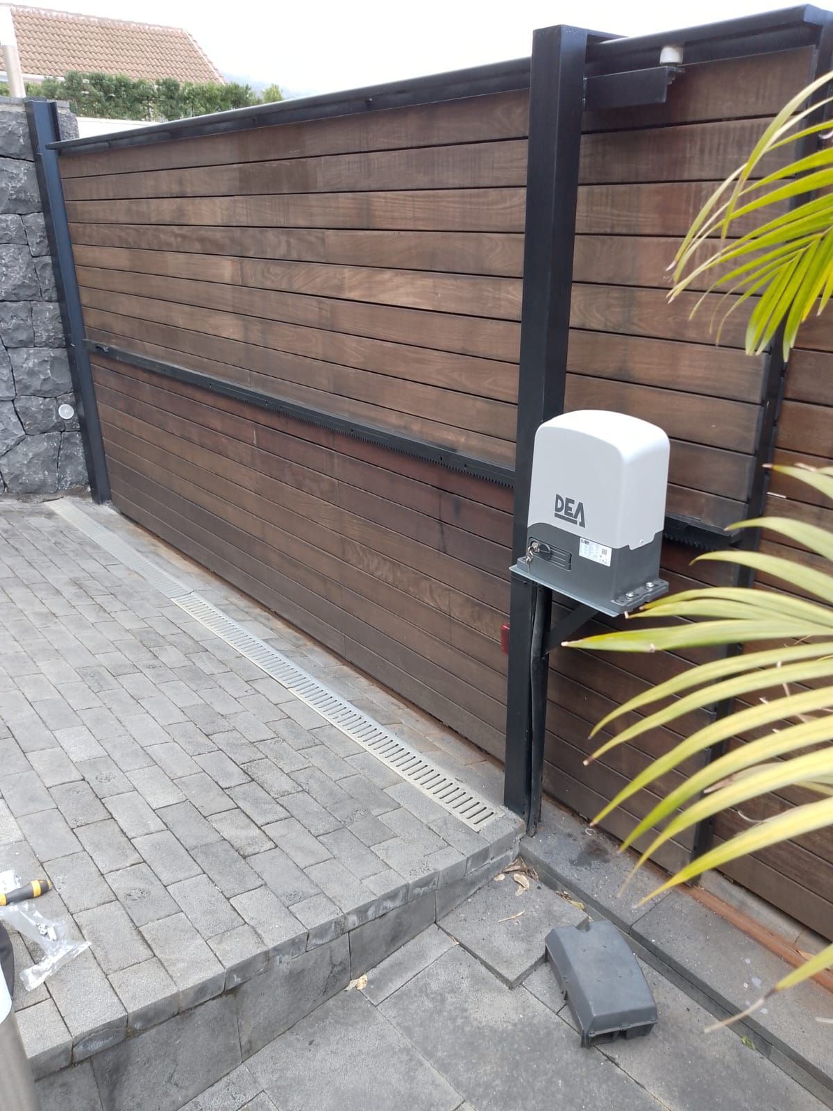 Una puerta de madera con abridor automático se encuentra en un camino de entrada pavimentado con ladrillos.