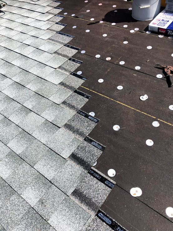A partially installed roof showing light gray asphalt shingles over black synthetic underlayment secured with white caps.