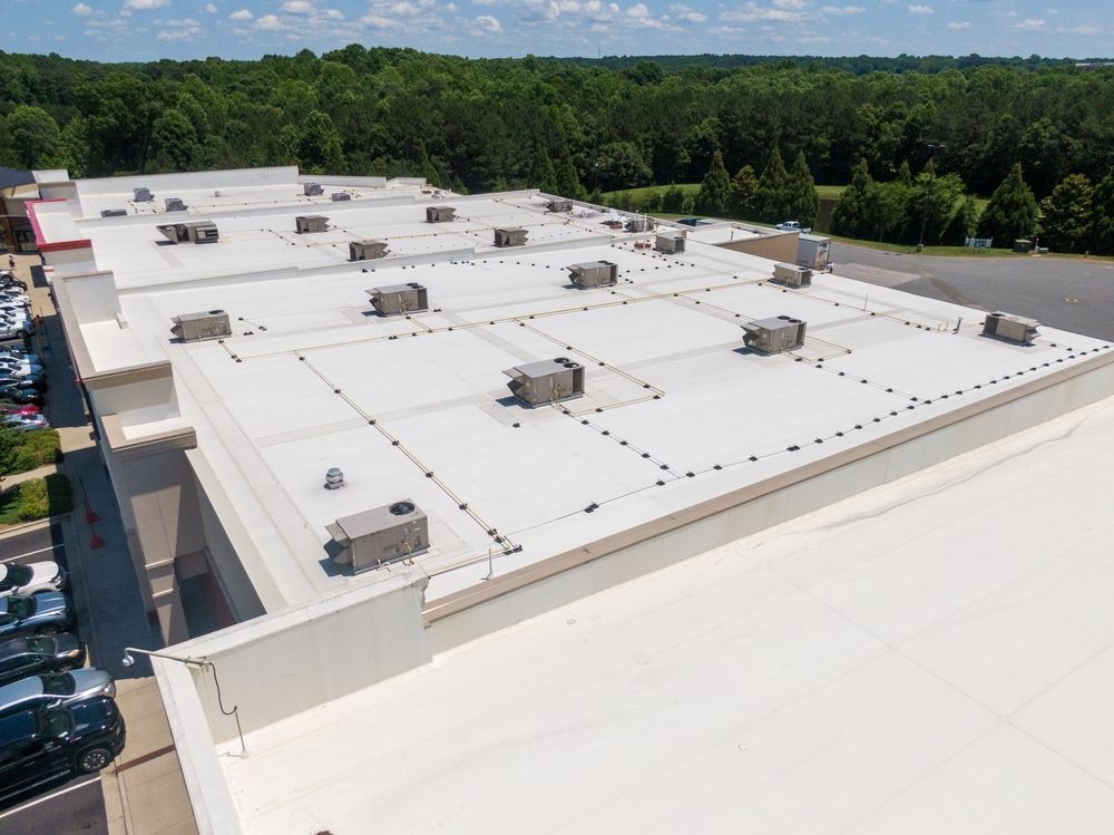 An aerial view of a flat commercial roof with multiple HVAC units and visible seam patterns, next to a parking lot.