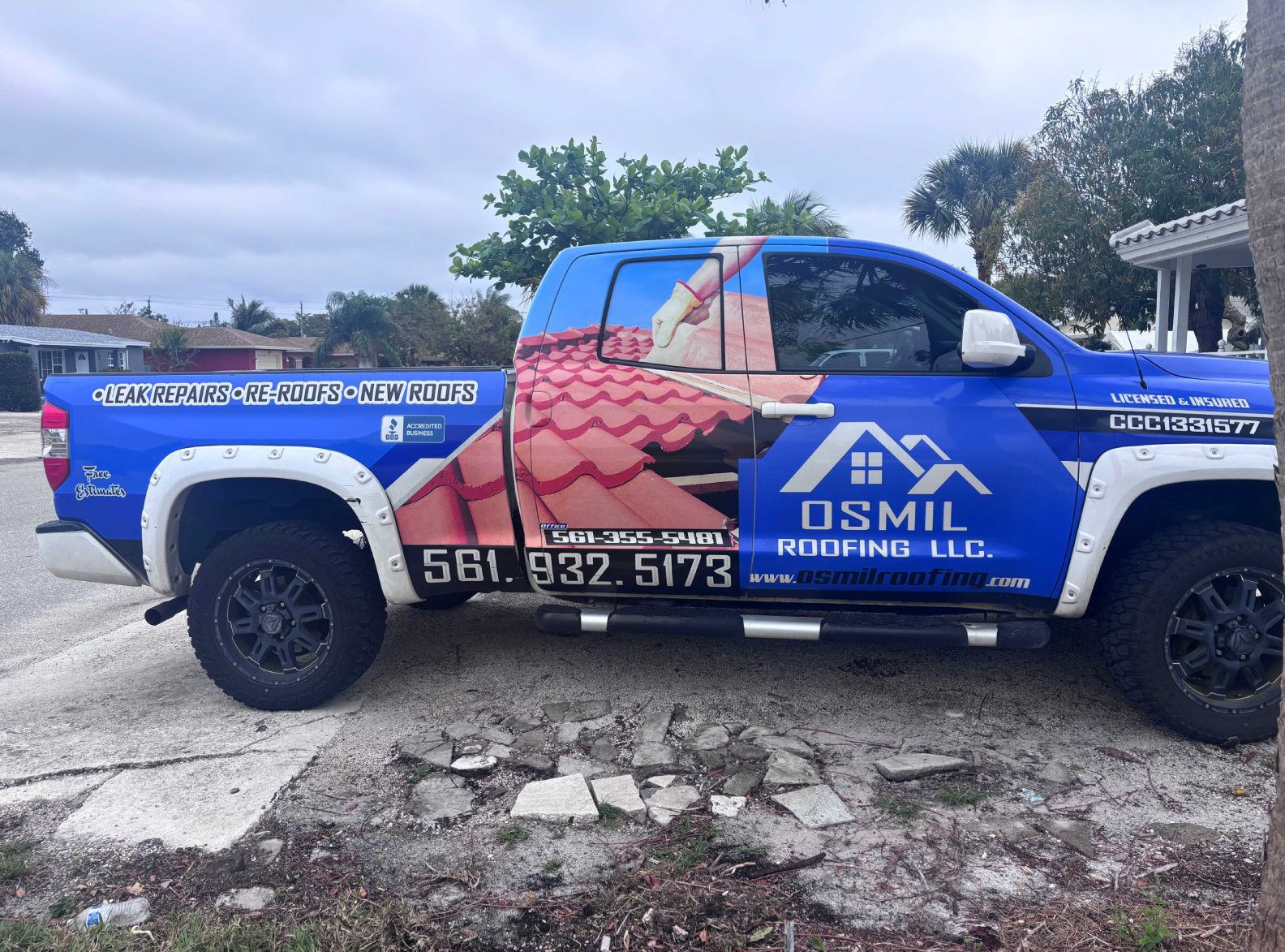 Blue Osmil Roofing LLC pickup truck parked on a paved lot, featuring a large graphic of red roof tiles and phone number.
