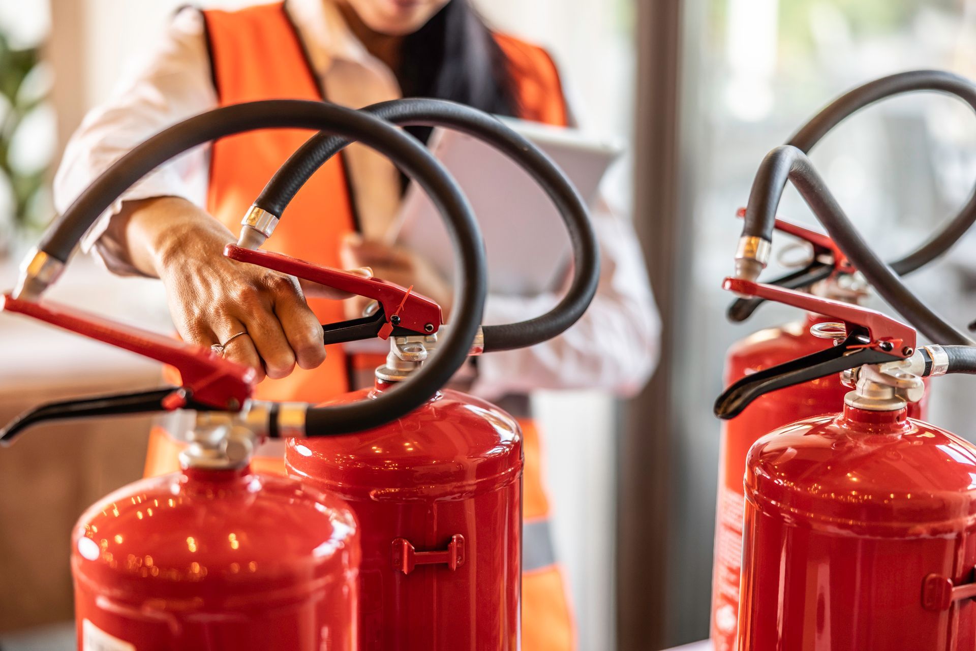 Worker in safety vest inspects fire extinguishers with clipboard during routine check.