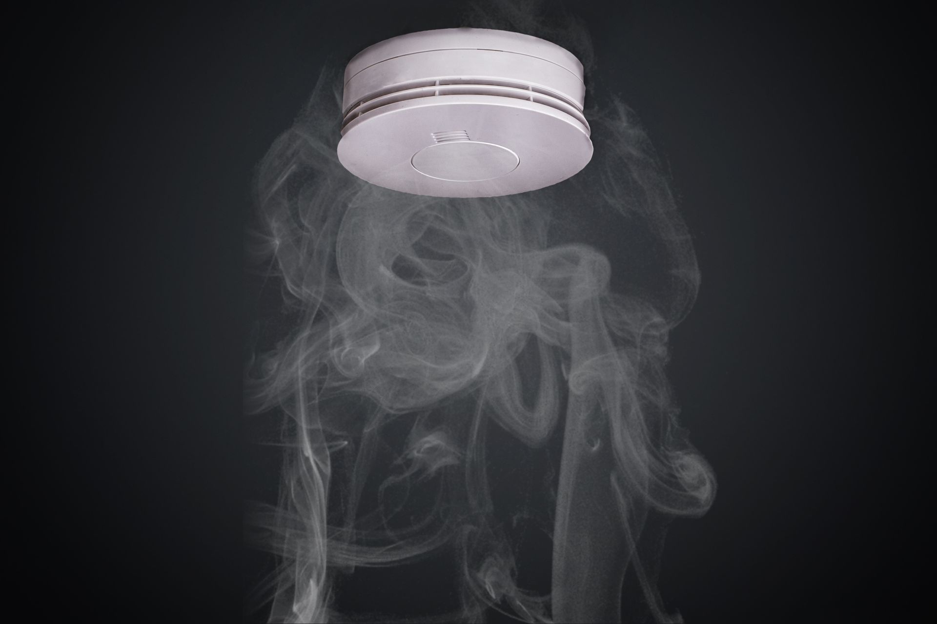 Smoke is coming out of a smoke detector on a black background.