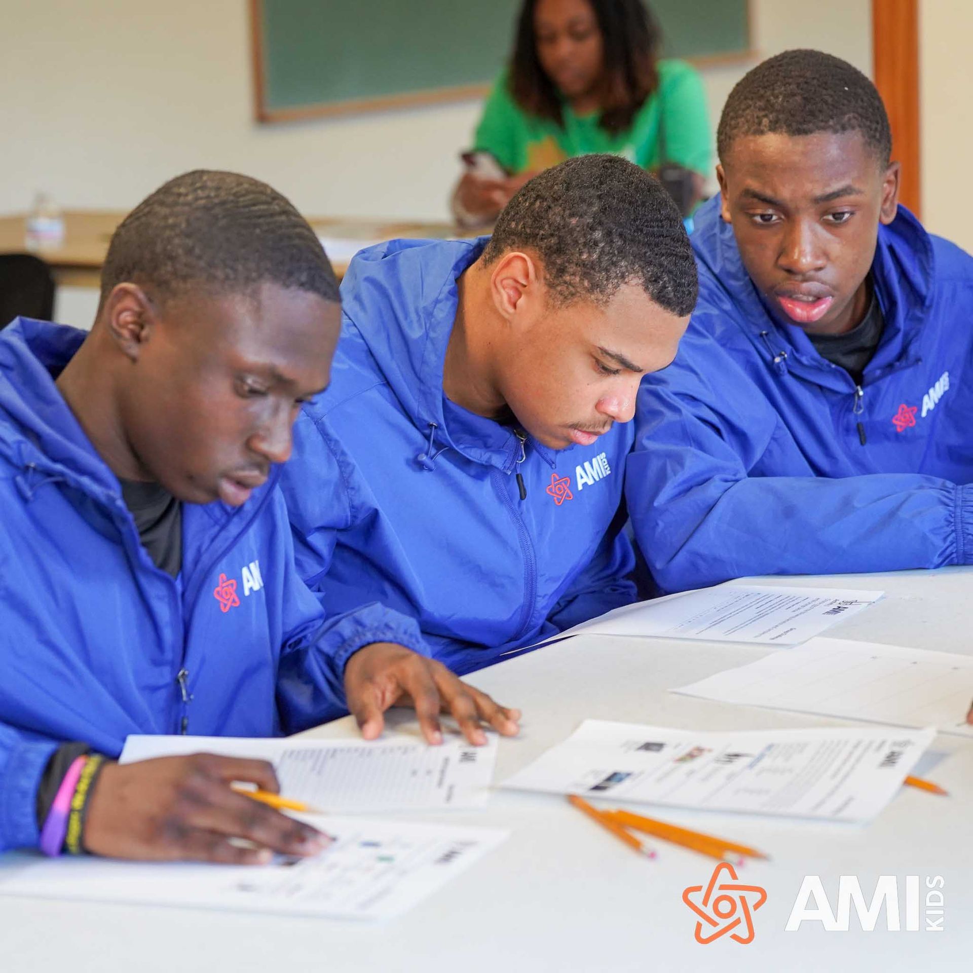Students in blue jackets studying paperwork together at a classroom desk
