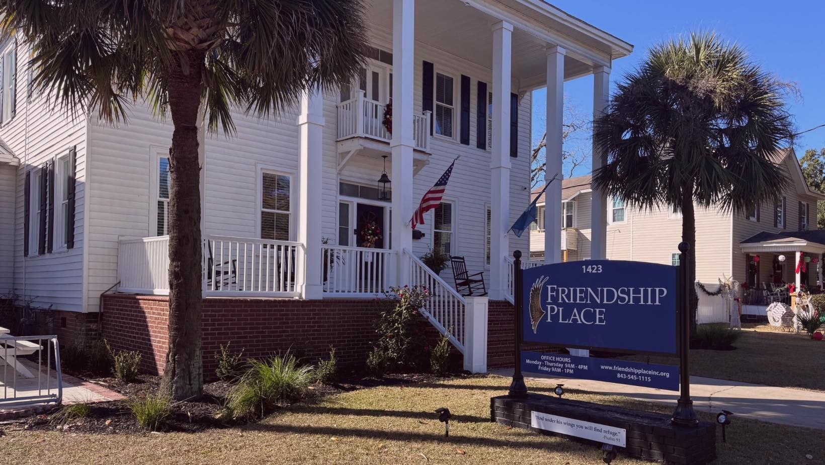 White house with porch and palm trees beside a sign reading