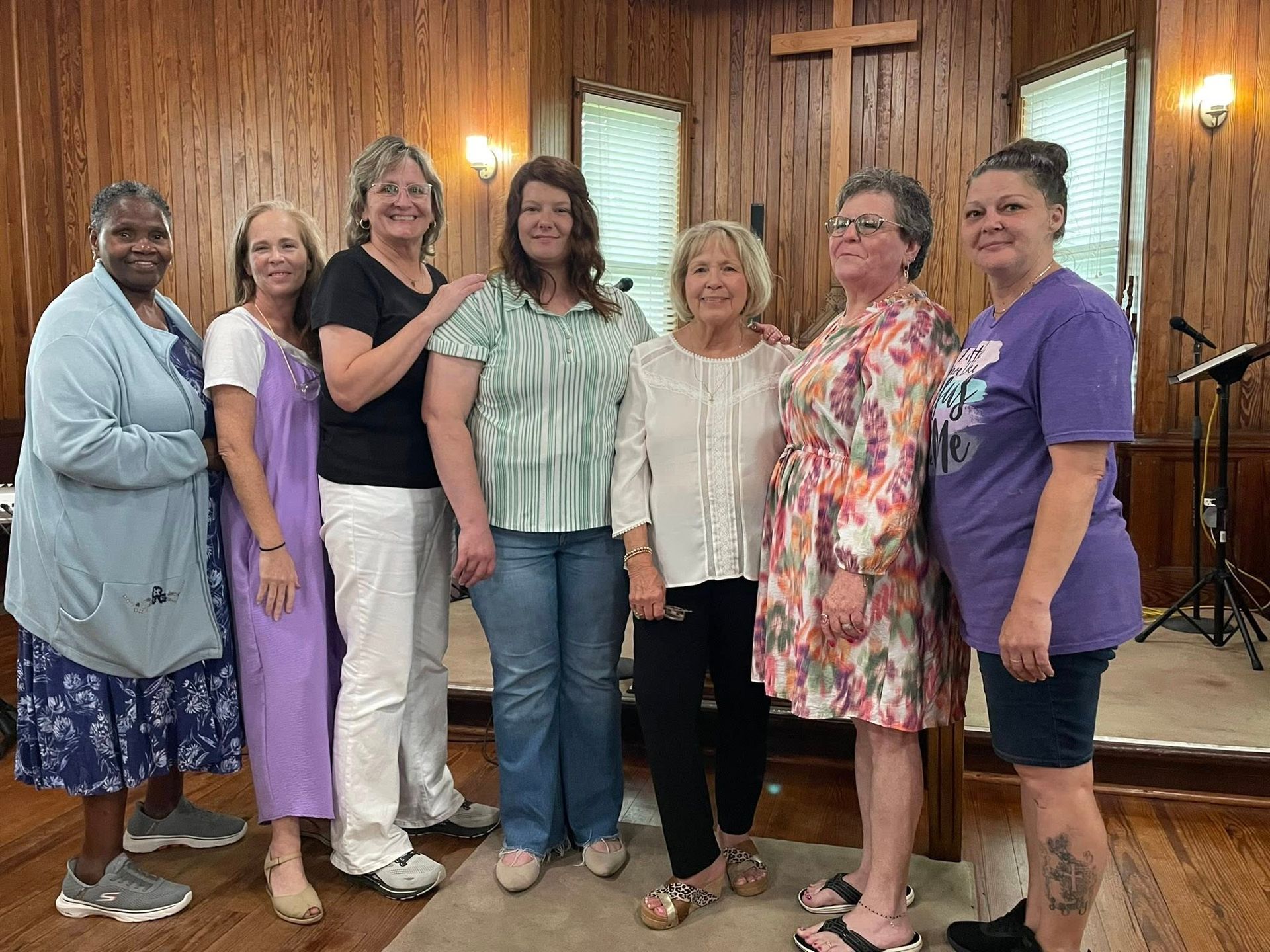 Six women pose together in a church sanctuary in front of a wooden cross.