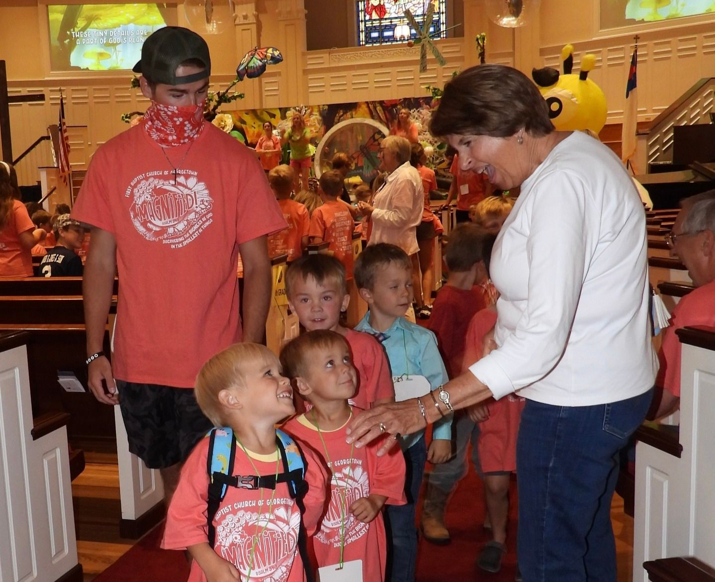 Family gathered in a restaurant as a woman greets children in the aisle, smiling and chatting.
