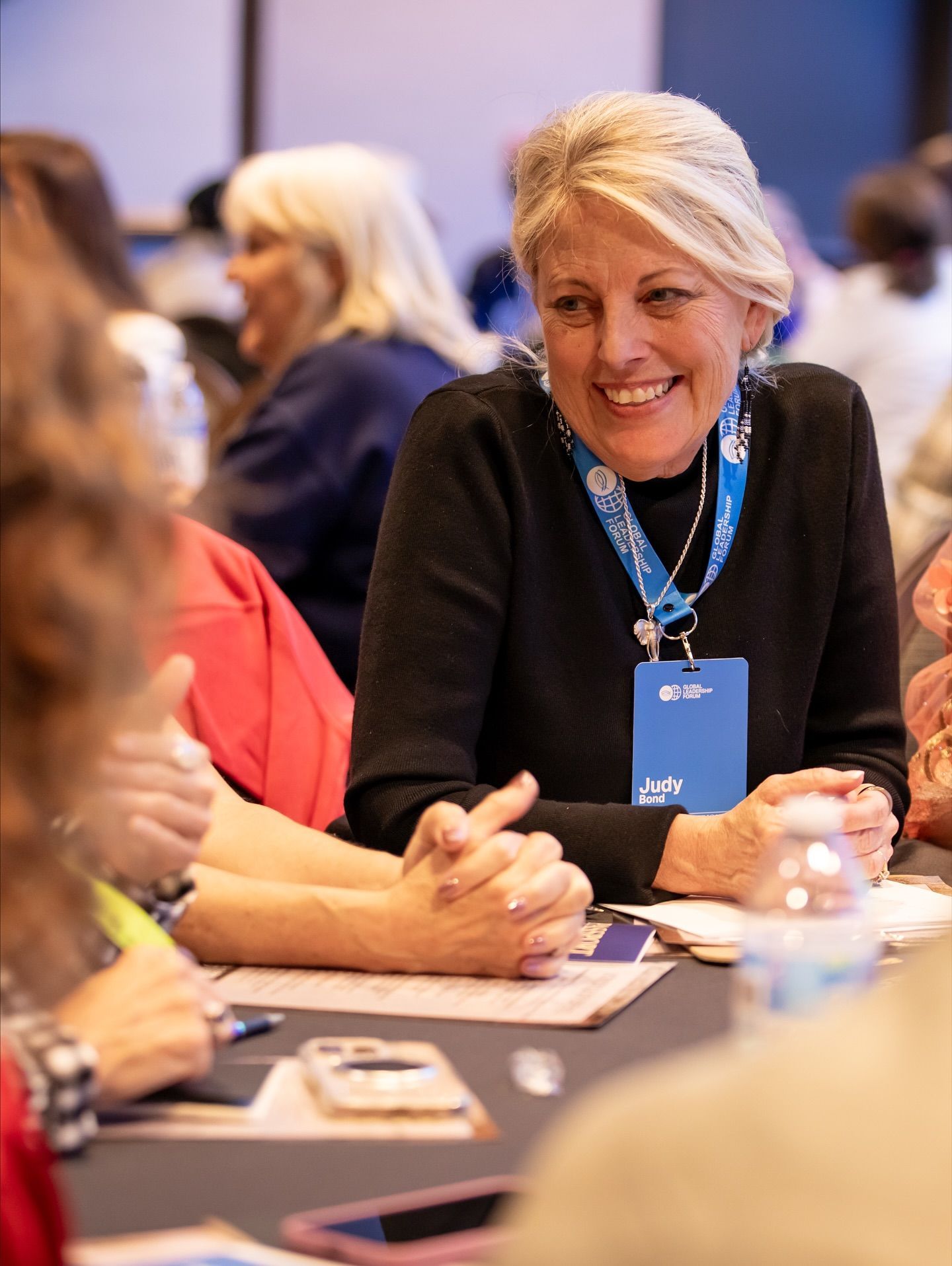 Smiling woman with a blue lanyard speaking at a conference table with others nearby