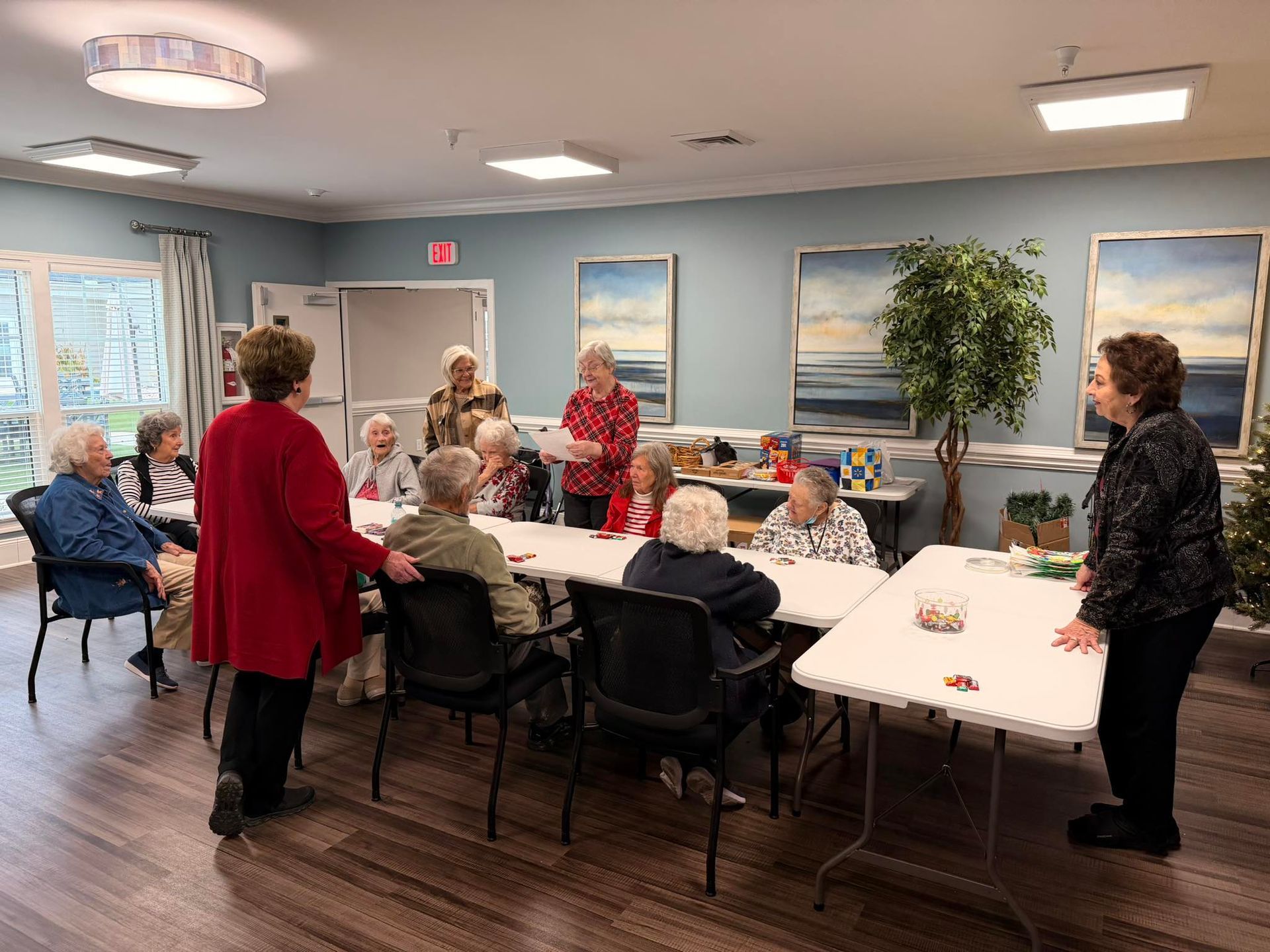 People gathered around a long table in a community room, with framed wall art and large windows.