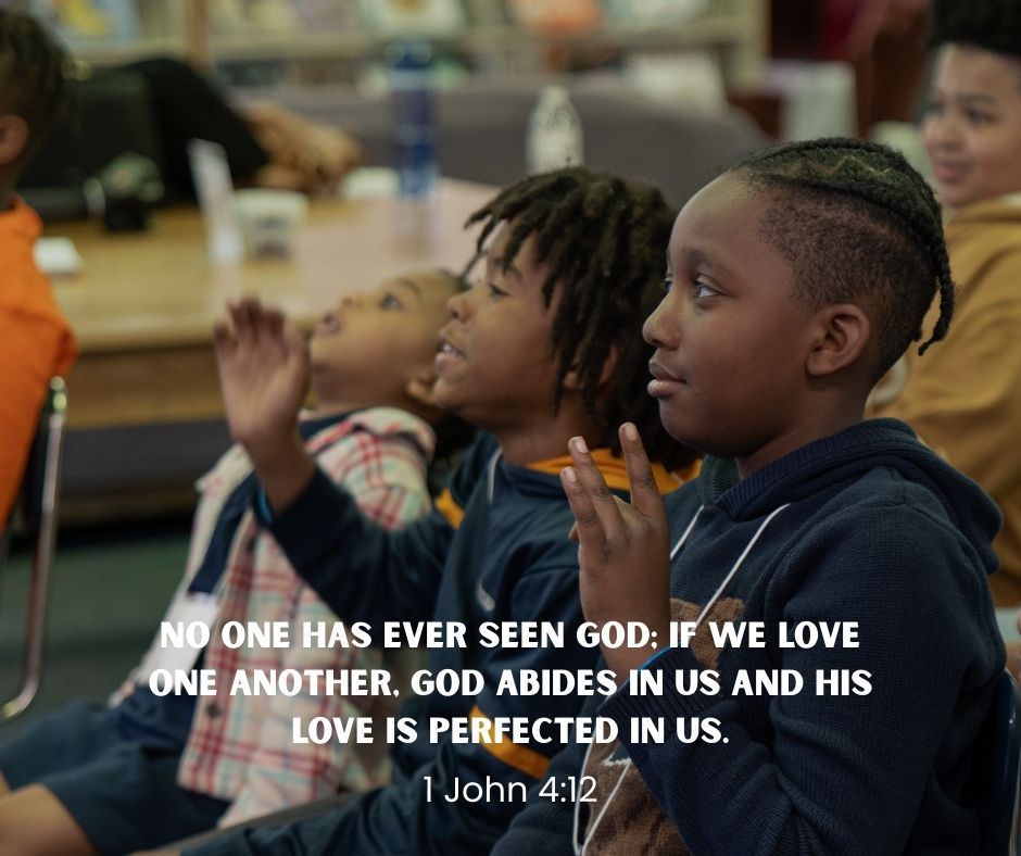 Children sit in a classroom, one clapping, with a Bible verse overlay about God’s love.