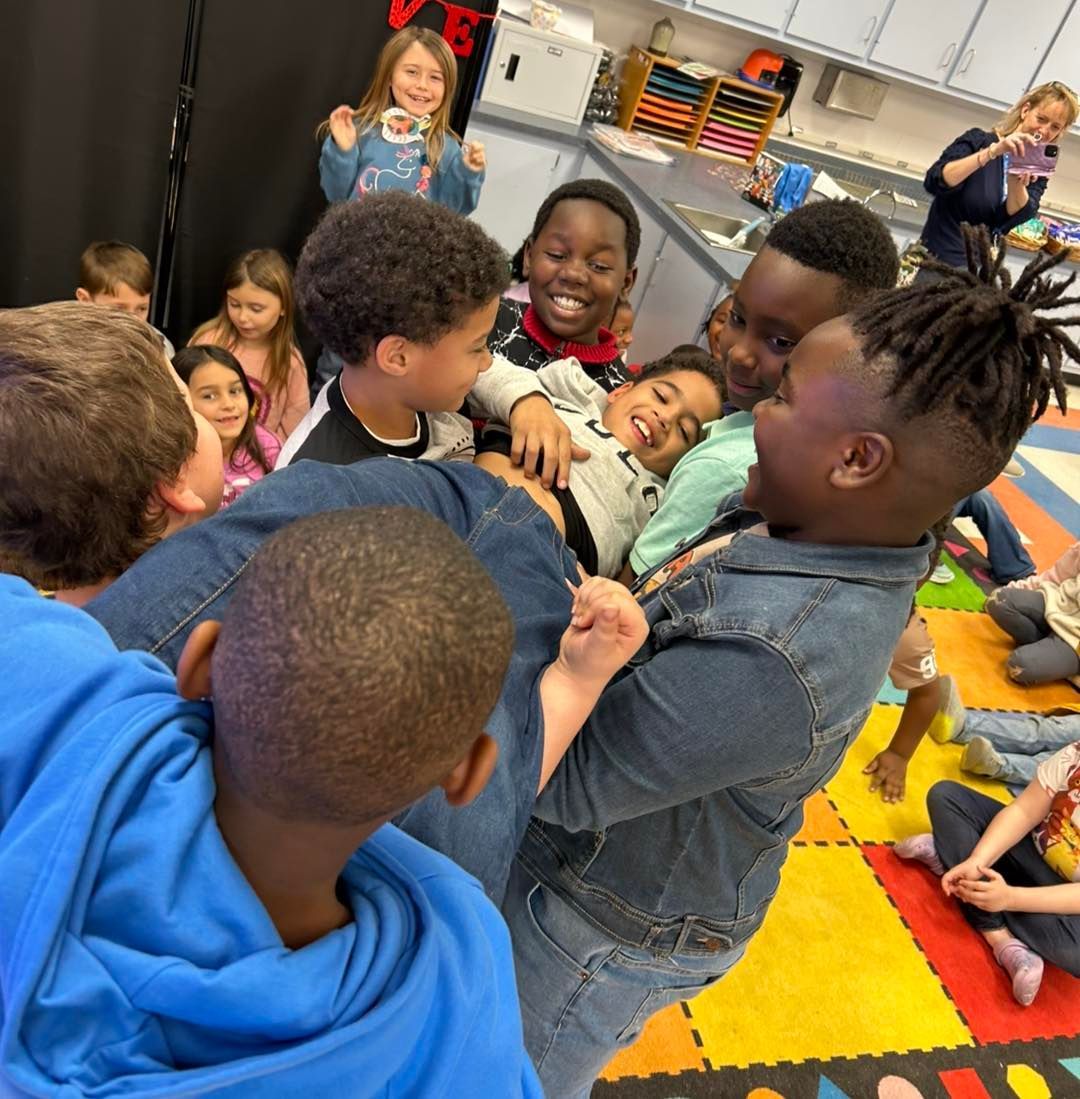 Children huddle together on a colorful classroom rug, smiling and laughing during a group activity.