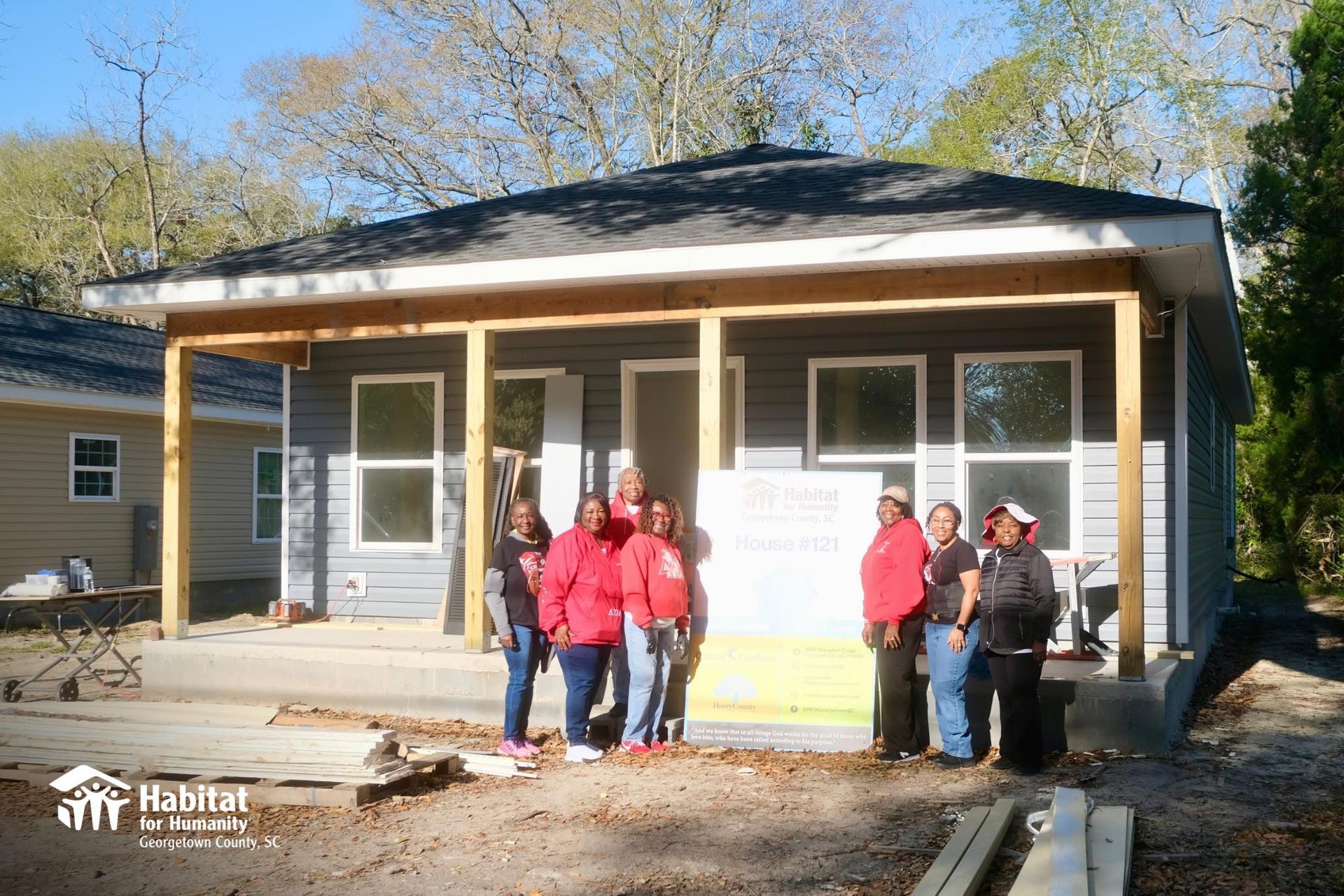 People standing in front of a small house under construction with a front porch and large windows.