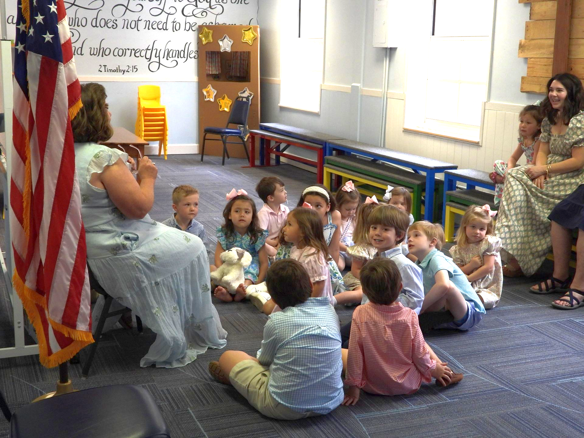 Teacher reads to children seated in a classroom circle with an American flag nearby