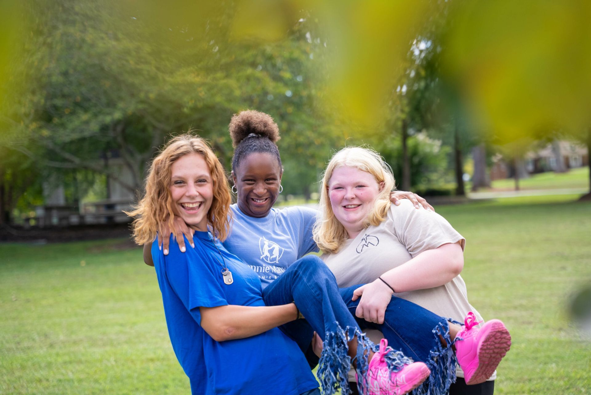 Three people smiling and posing together in a park, with two being held up in arms