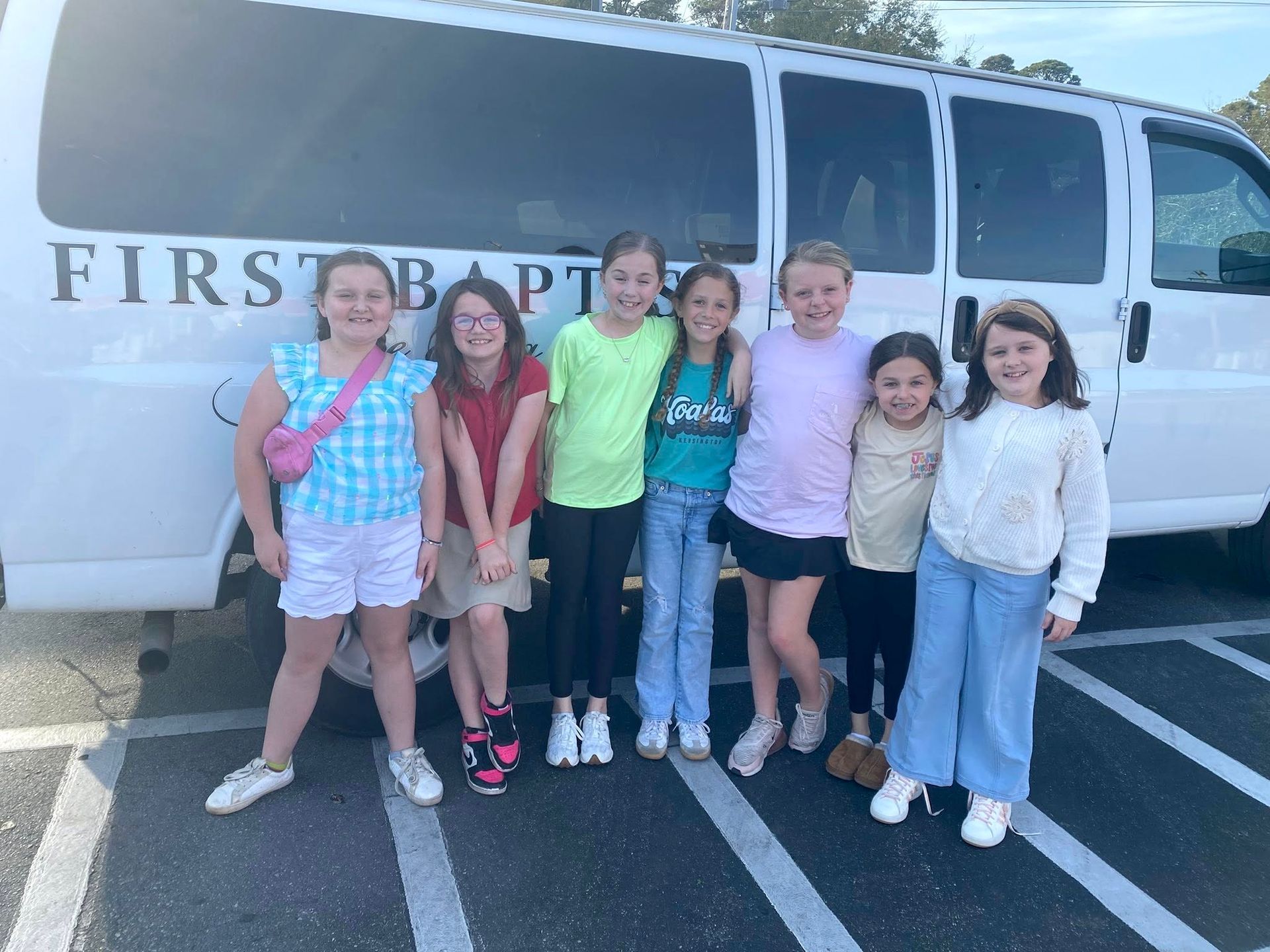 Six smiling youths stand in a parking lot in front of a white First Baptist van.