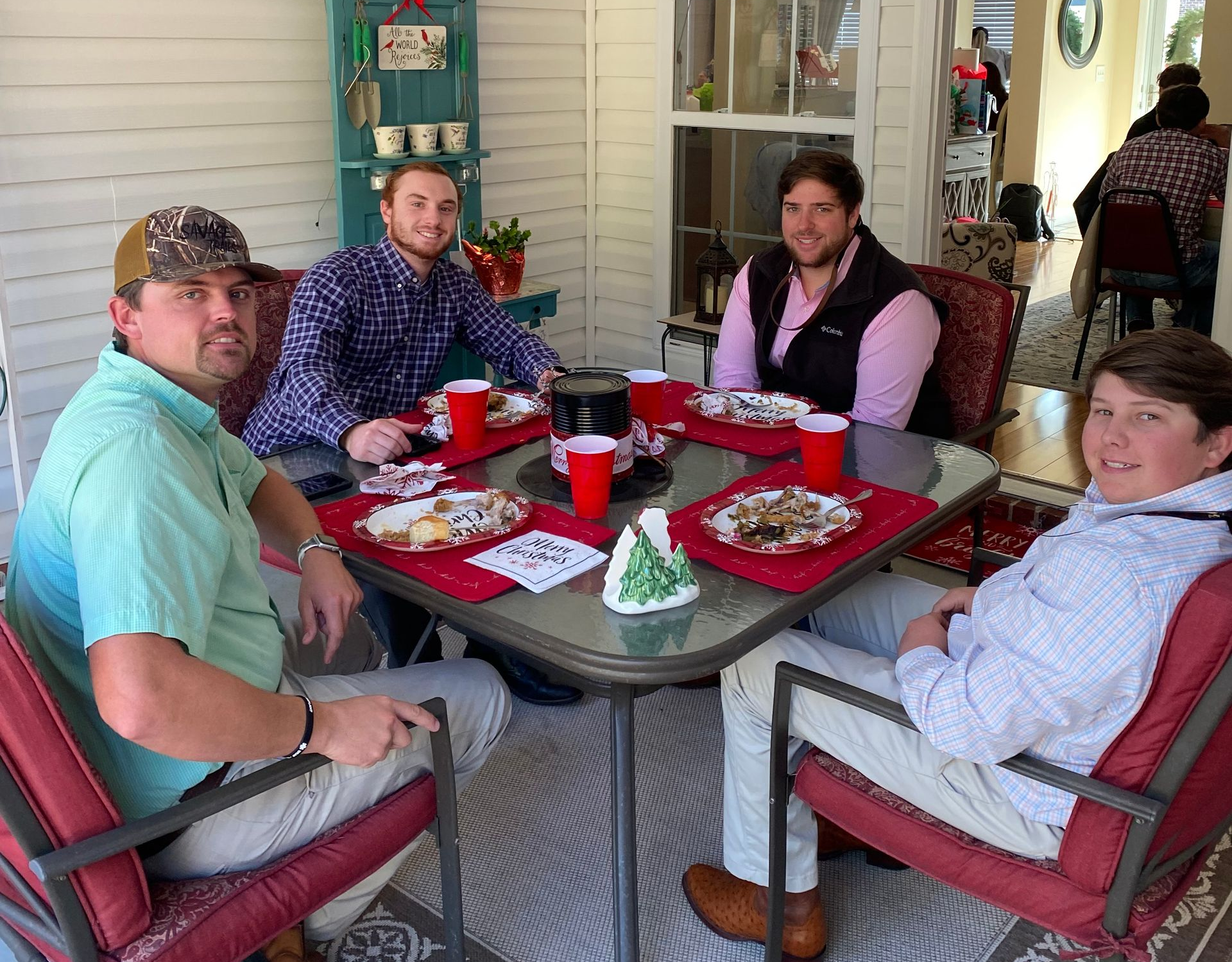 Four people seated around a red-set patio table, smiling and dining outdoors at a restaurant.