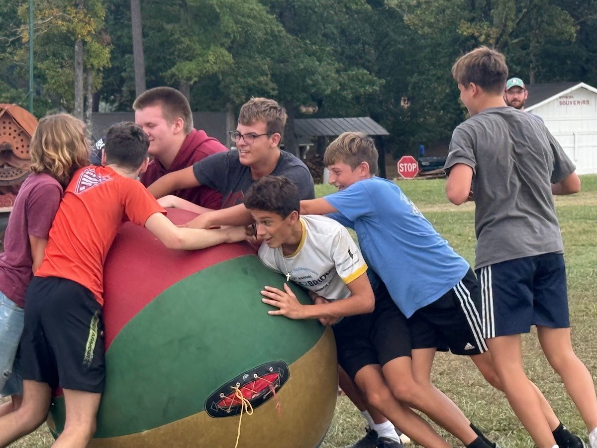 People pushing a large red and green exercise ball outdoors on a grassy field
