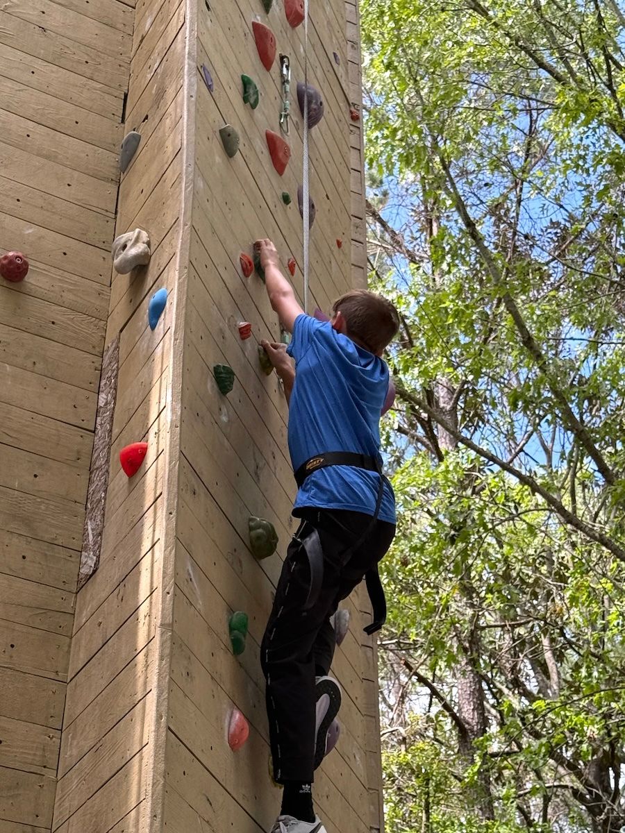 Person climbing an indoor rock wall with colorful holds outdoors near trees