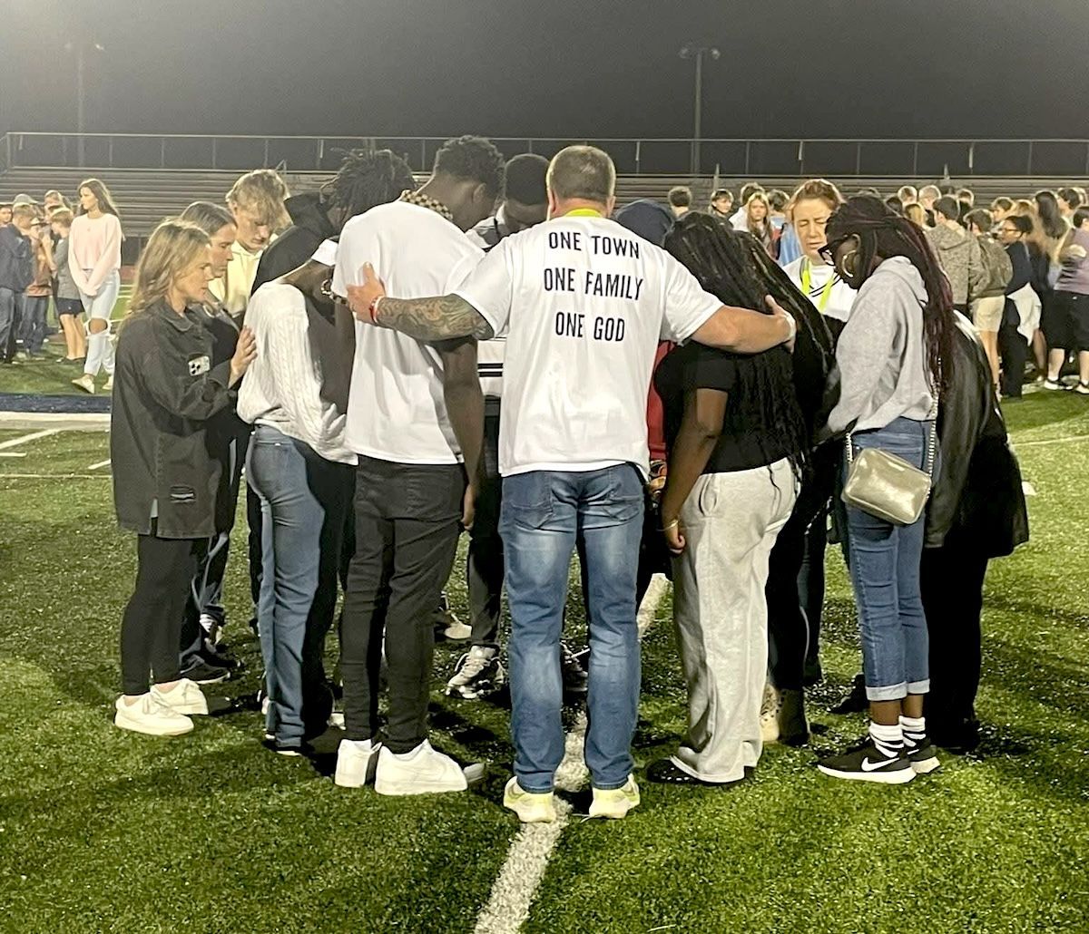 Group of people standing in a circle on a lit sports field at night, gathered in team huddle