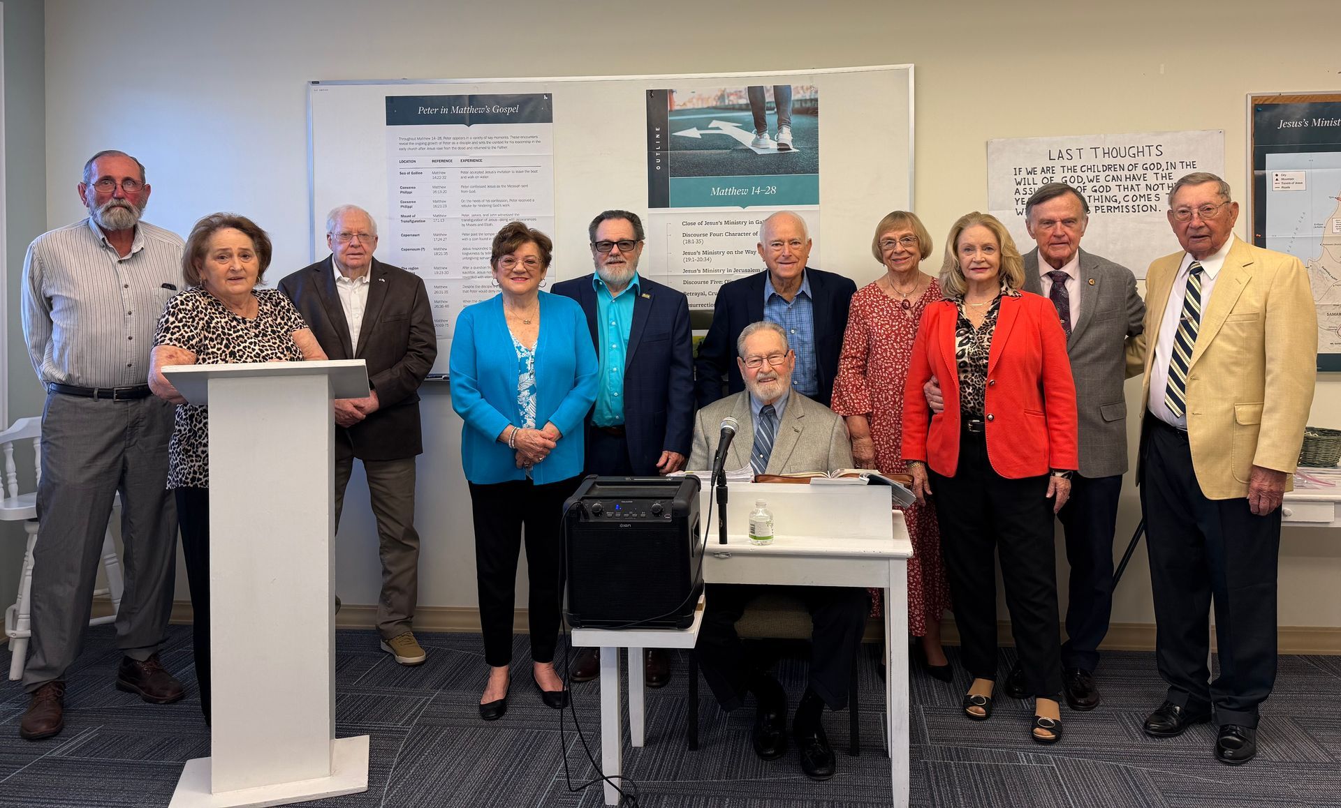 Group of people posing at a podium in a conference room, with a seated man at a small table in front