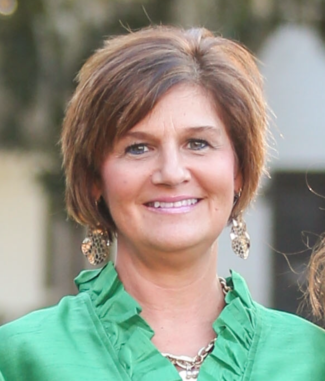 Smiling woman in a green blouse and statement earrings outdoors