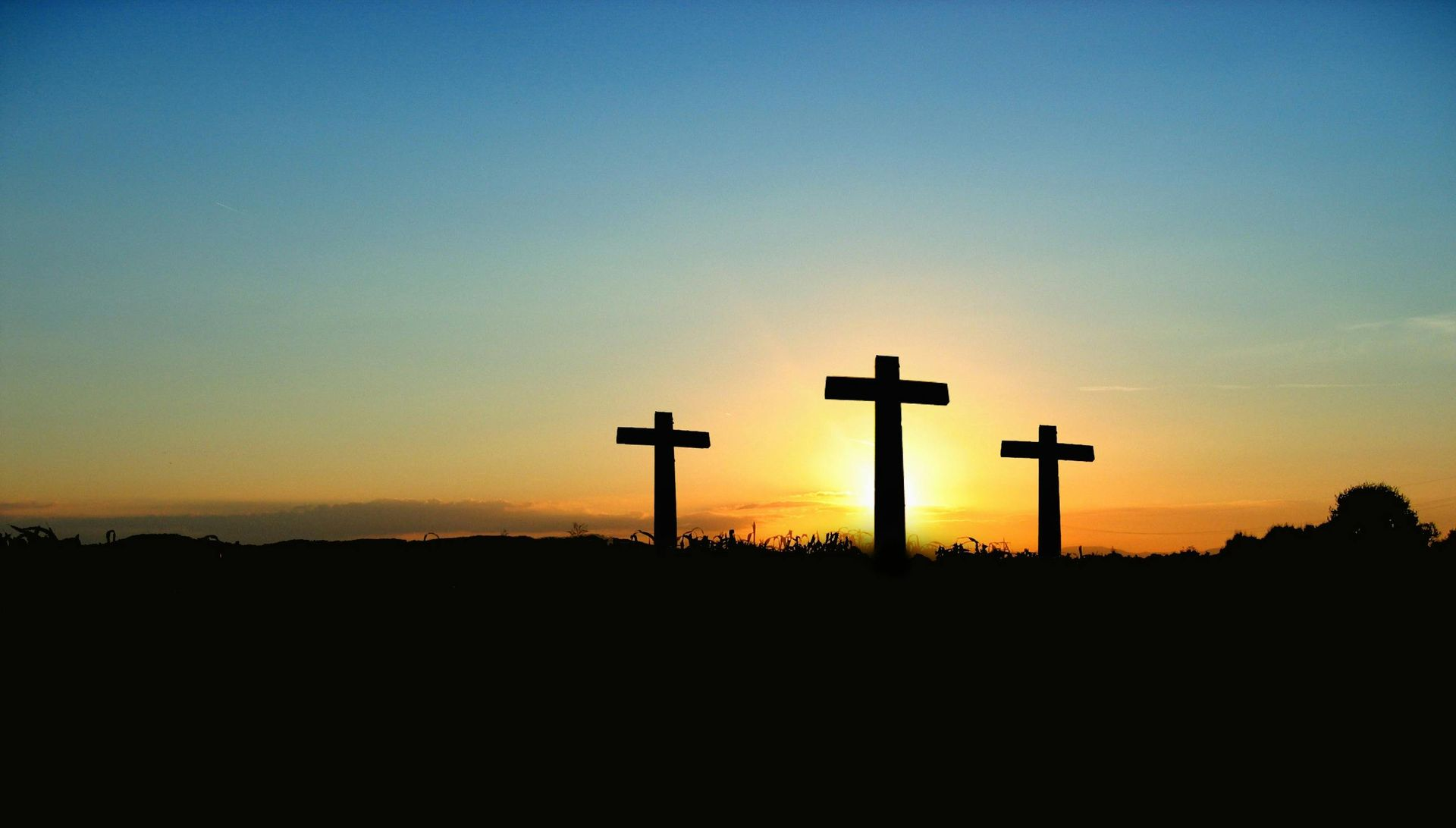 Three crosses silhouetted against a sunset sky over a dark horizon