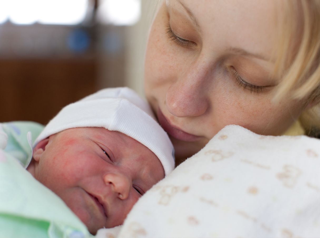 Sleeping newborn in white hat cuddled close to a resting parent in a soft blanket