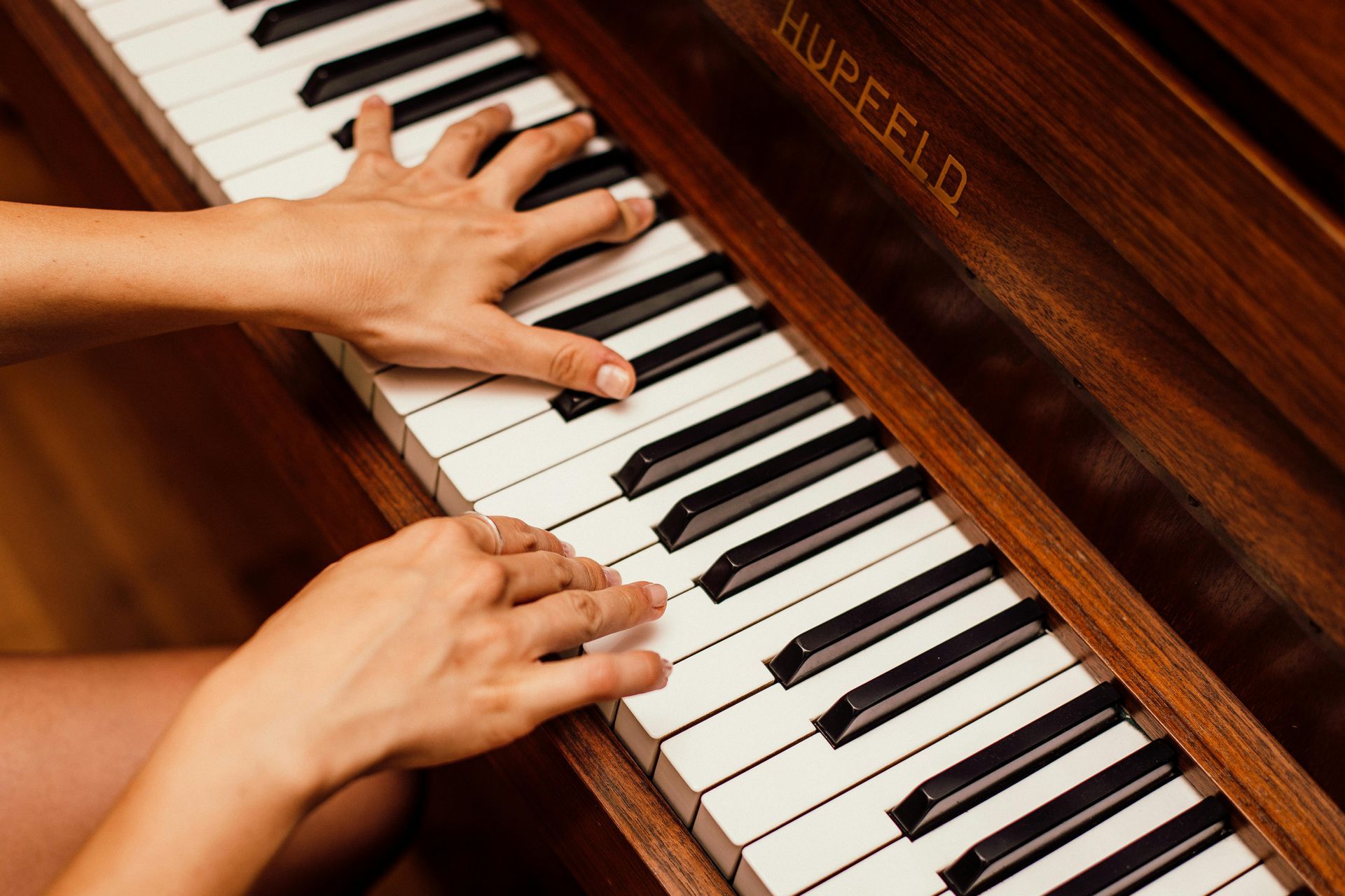 Two hands playing a piano keyboard with a wooden finish