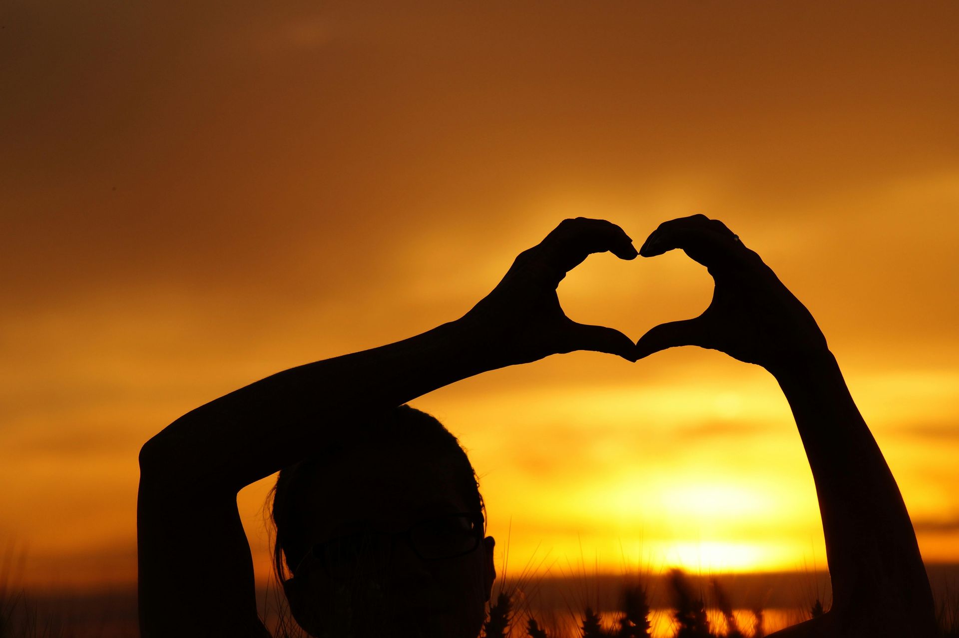 Silhouette of two hands forming a heart against a golden sunset sky