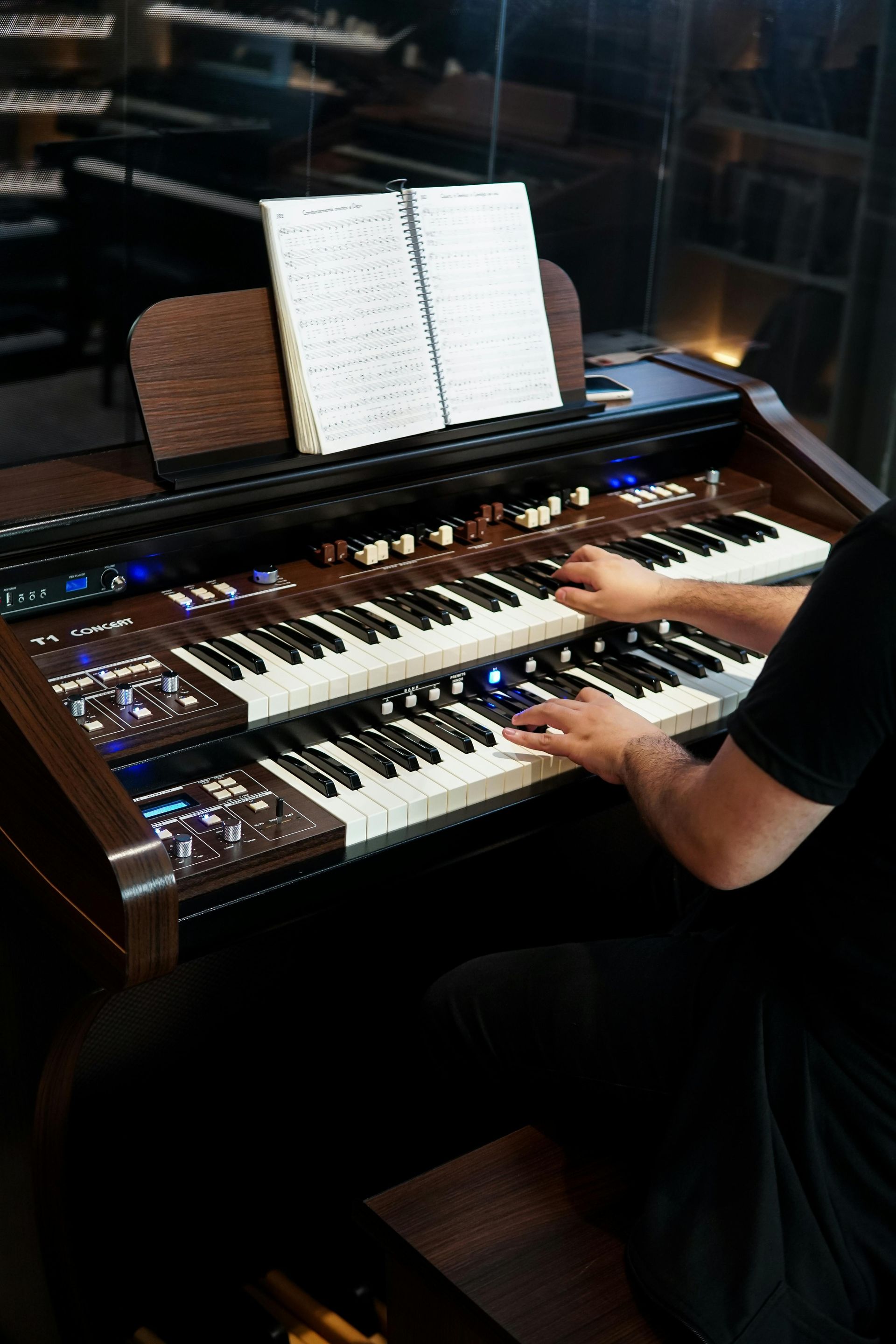 Person playing a dual-manual organ with sheet music in a dimly lit room