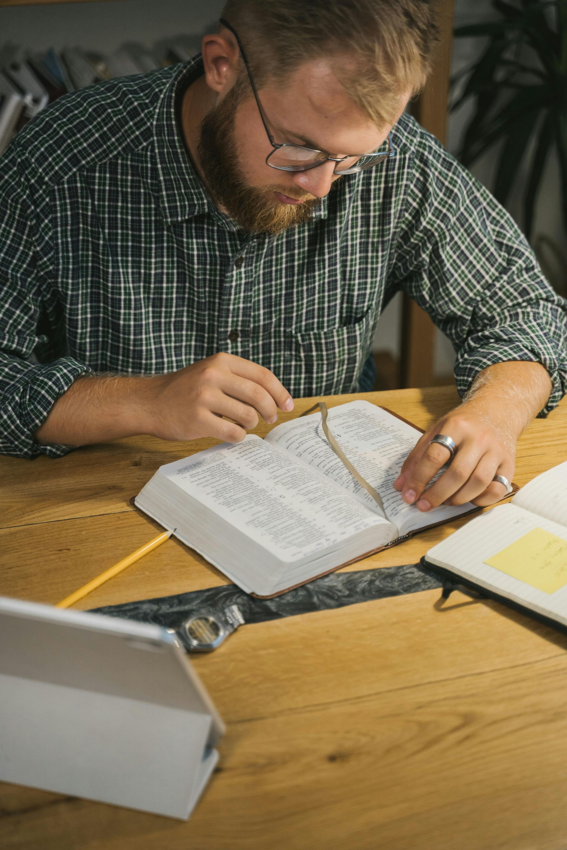 Man studying at a desk, reading papers and writing notes beside a laptop.