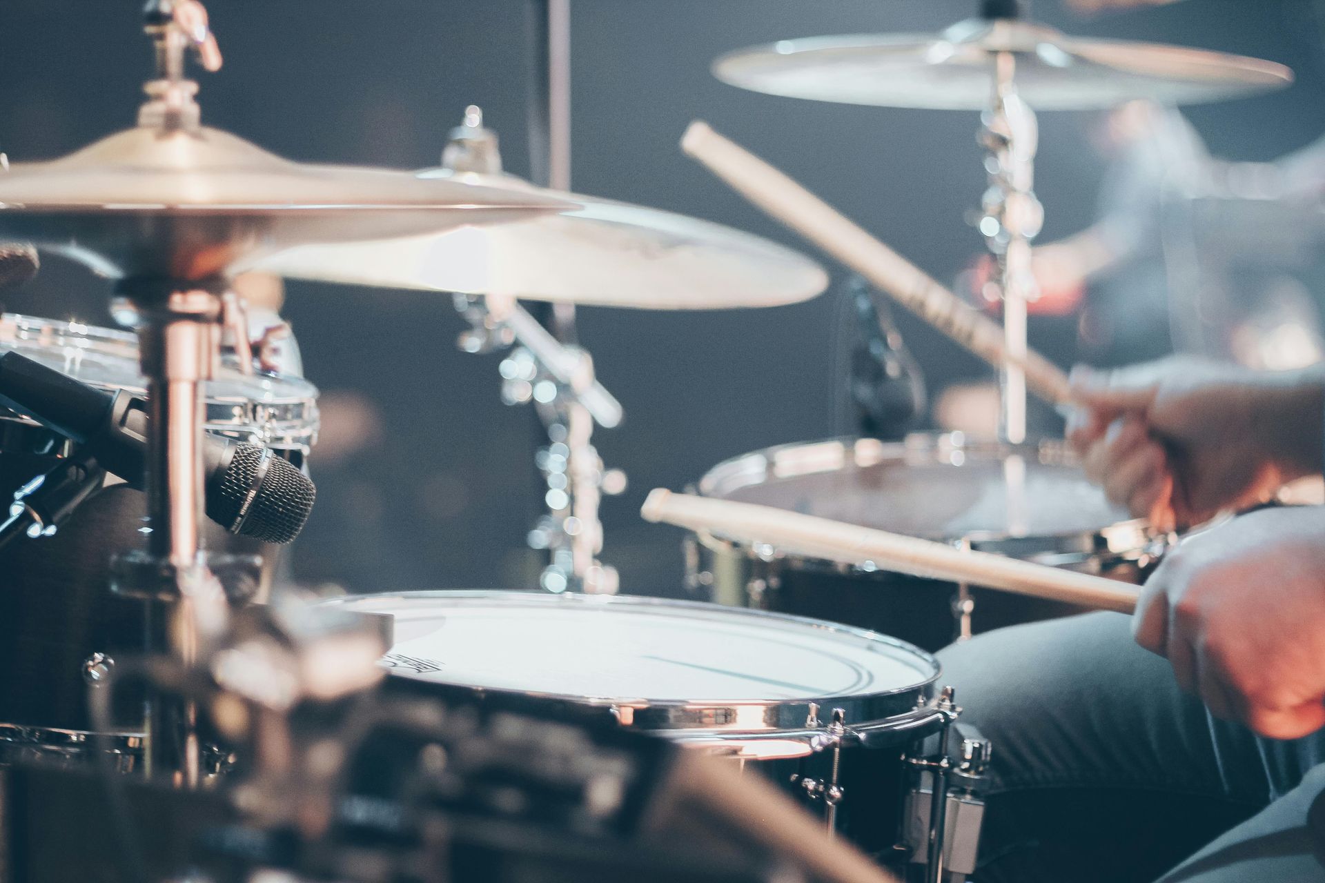Drummer playing a drum kit with cymbals on a stage, close-up view of hands and drums