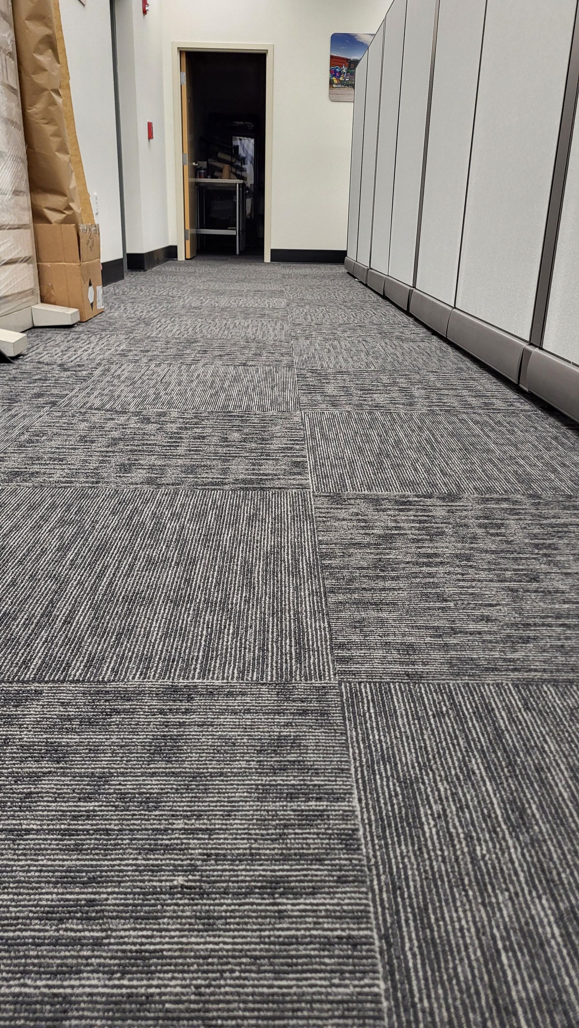 A long hallway with a carpeted floor and a door leading to a room.