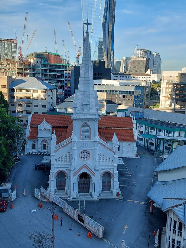 White church with a tall steeple in a city, surrounded by buildings and construction.