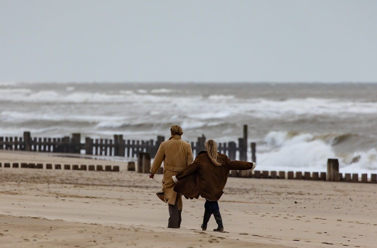 Een man en een vrouw lopen op een strand bij de oceaan
